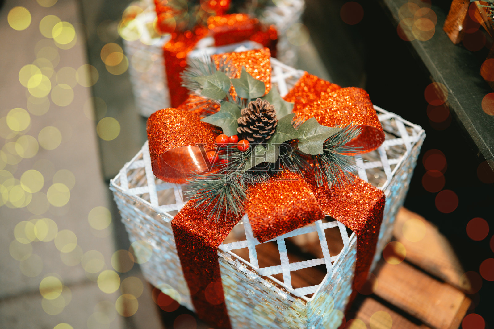 带有红色闪光蝴蝶结和松果的装饰礼品盒。柔和的散景灯光营造出节日氛围。照片摄影图片