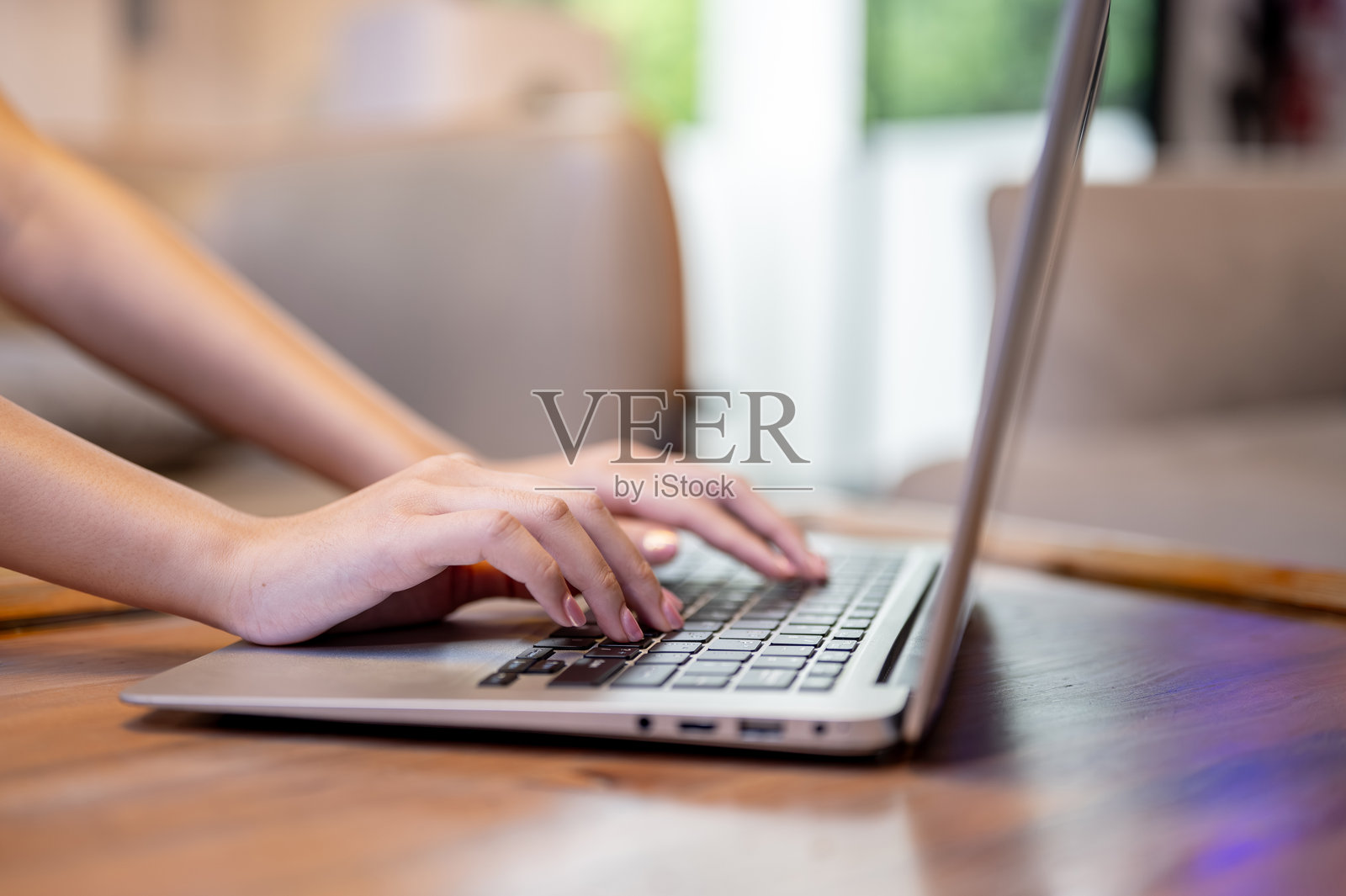 特写女性双手在客厅或咖啡馆的木桌上敲击笔记本电脑照片摄影图片