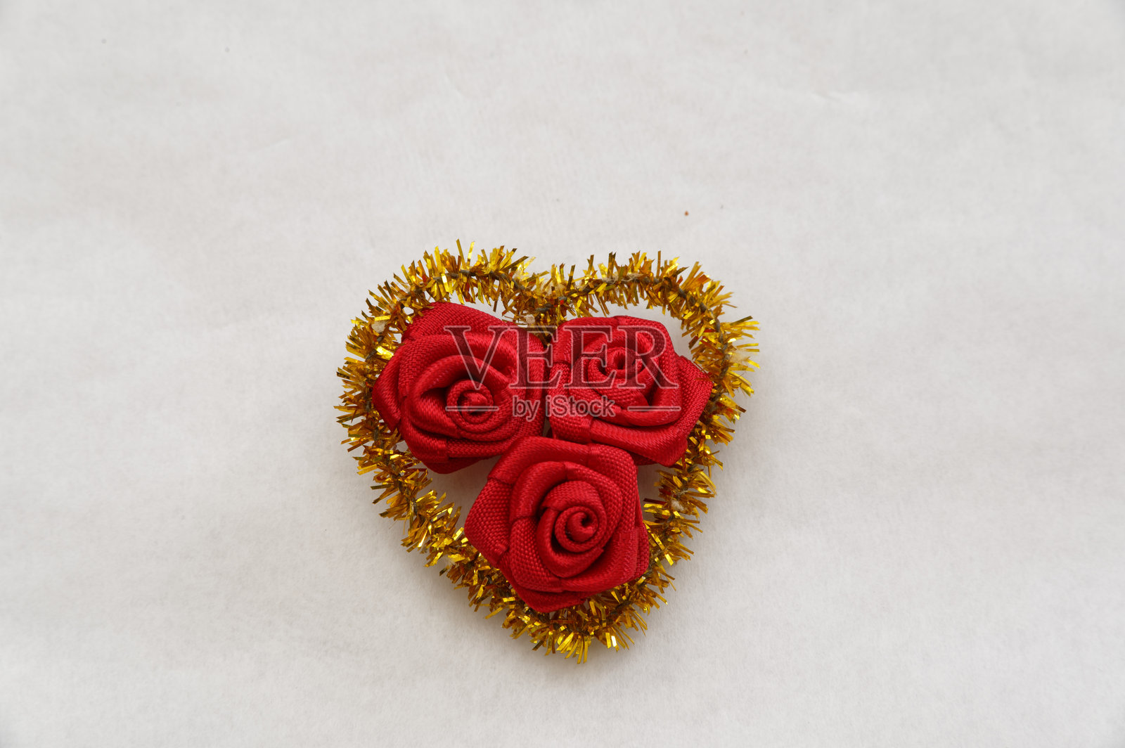 由材料制成的三朵小红玫瑰,坐落在一个金色的闪光的心形中。照片摄影图片