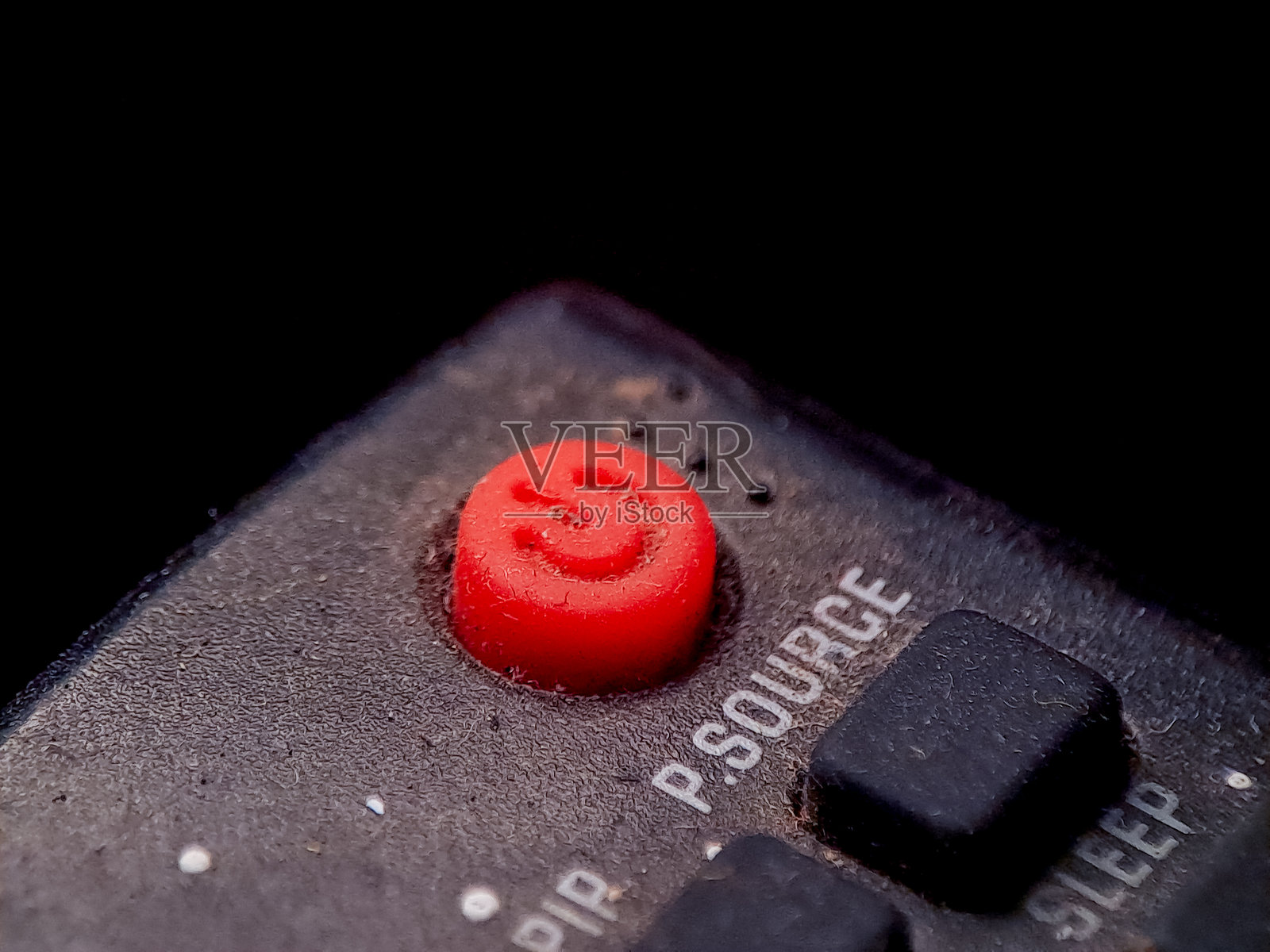 特写镜头,展示了带有粗糙纹理表面的遥控器上的红色电源按钮。照片摄影图片