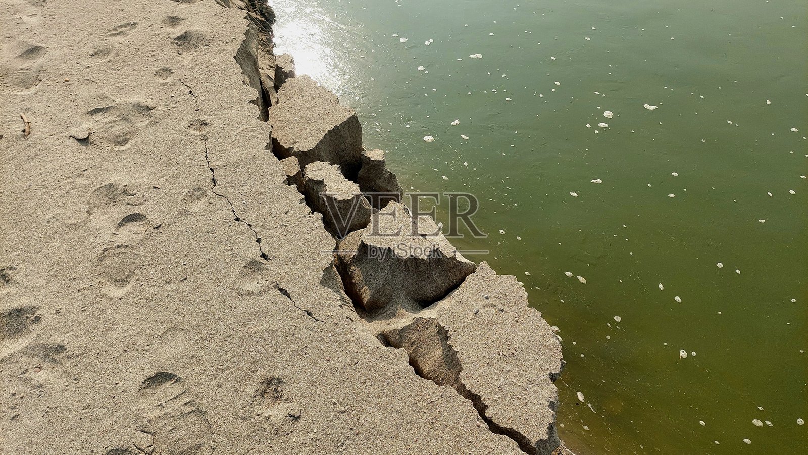 河岸严重侵蚀,边缘开裂,旁边是平静的绿水照片摄影图片