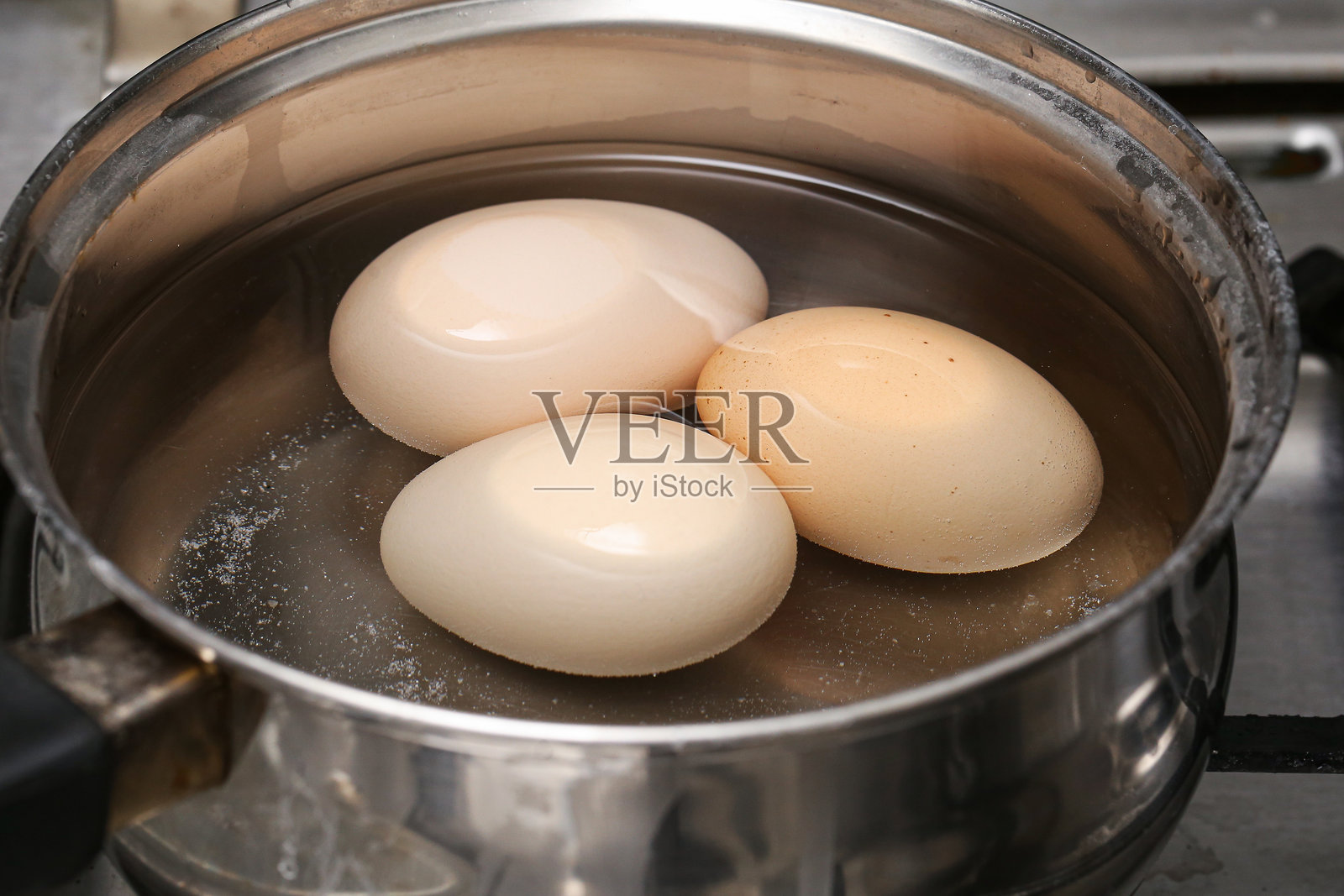 在燃气灶上的锅里煮鸡蛋。在厨房里烹饪早餐。照片摄影图片