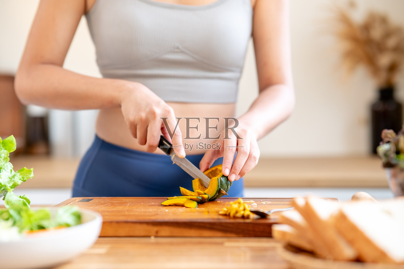 特写:身穿运动服的女性在厨房料理台的砧板上持刀切南瓜照片摄影图片