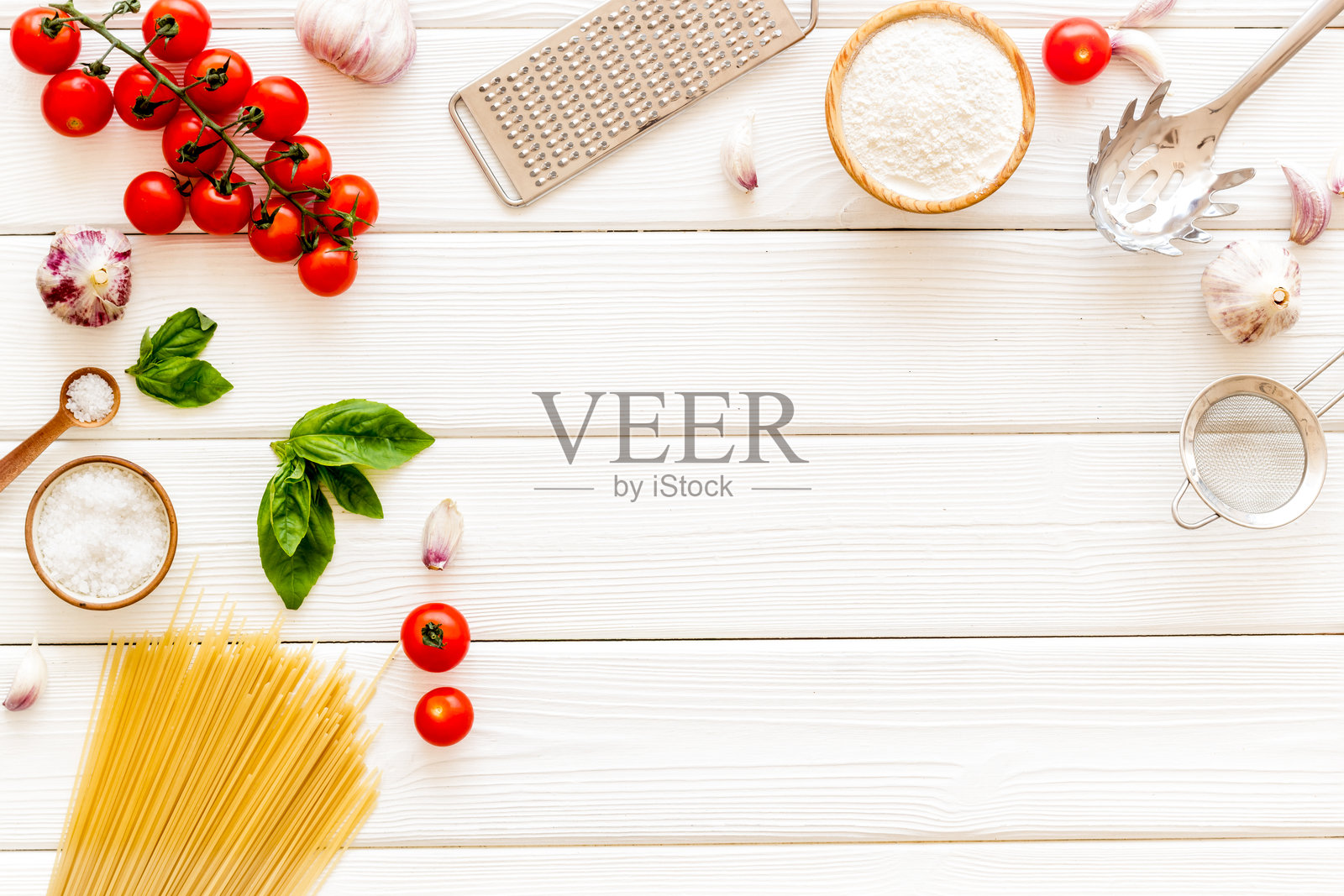 俯视角度,白色木质背景上铺着未煮的意大利面,配有制作意大利面食的食材——番茄、罗勒和大蒜。照片摄影图片