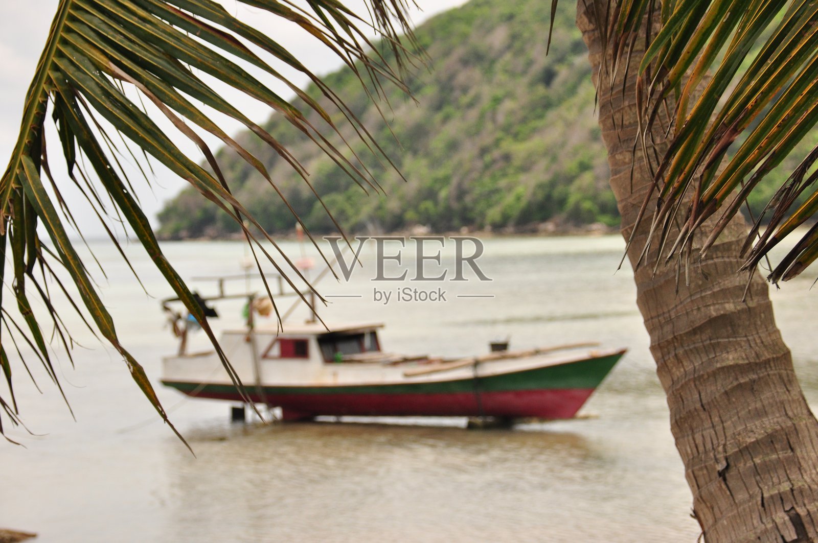 宁静的一天,一艘渔船停泊在热带海滩附近,周围环绕着郁郁葱葱的绿色山丘。照片摄影图片
