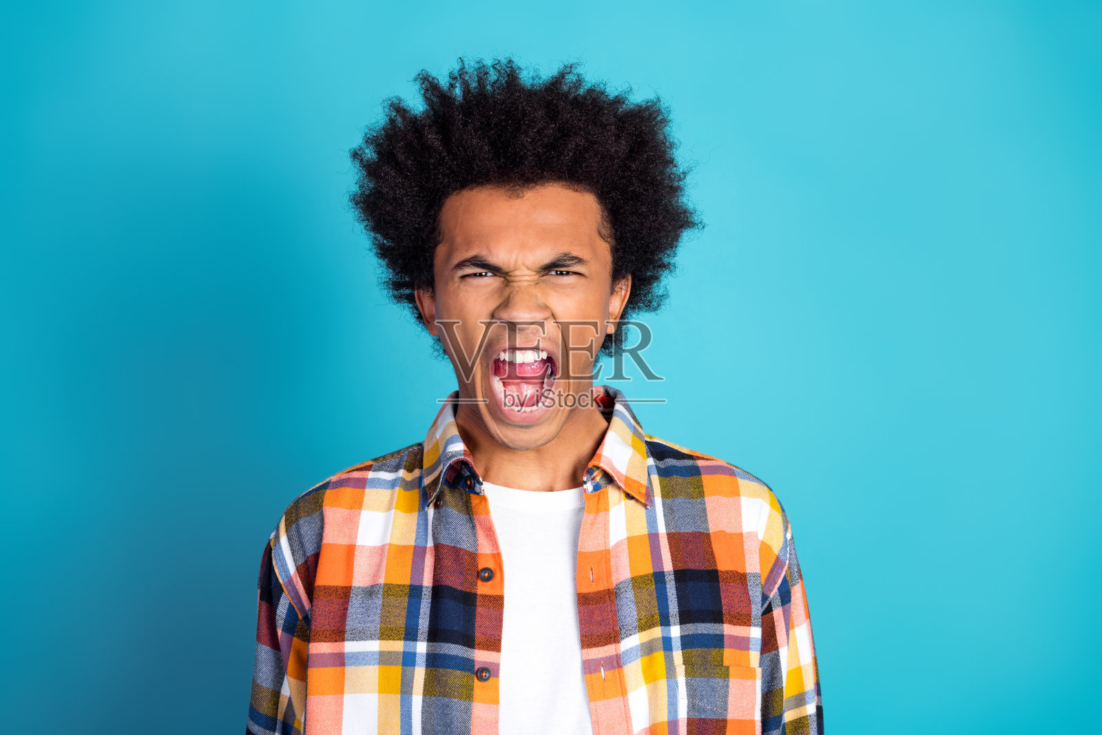 身穿彩色格子衬衫的年轻男子在蓝色背景前做出夸张的呐喊表情照片摄影图片