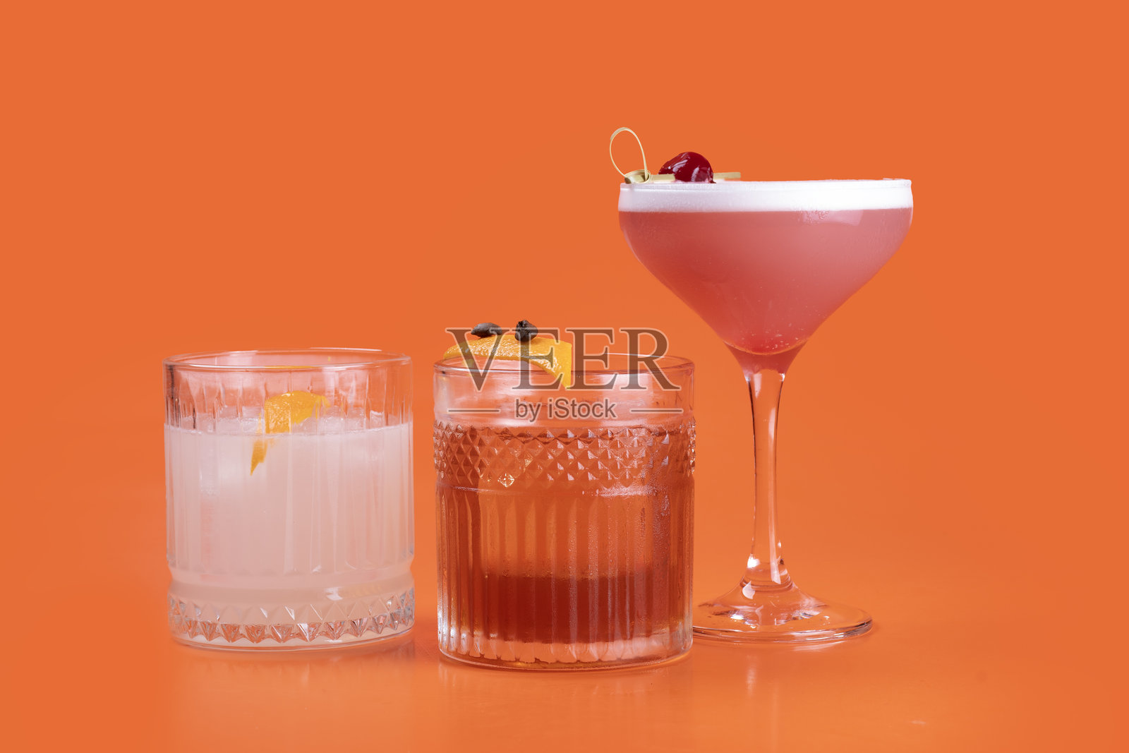 橙色背景上的三杯色彩缤纷的鸡尾酒,科斯莫波利坦热带饮品照片摄影图片