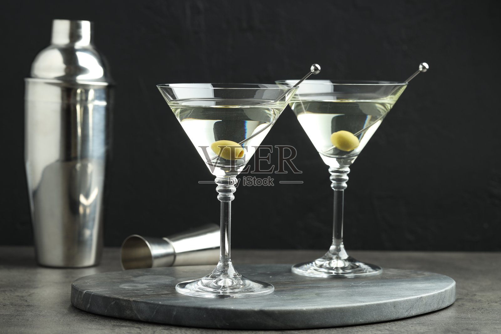 灰色桌面上放着马提尼鸡尾酒和橄榄,背景为黑色照片摄影图片