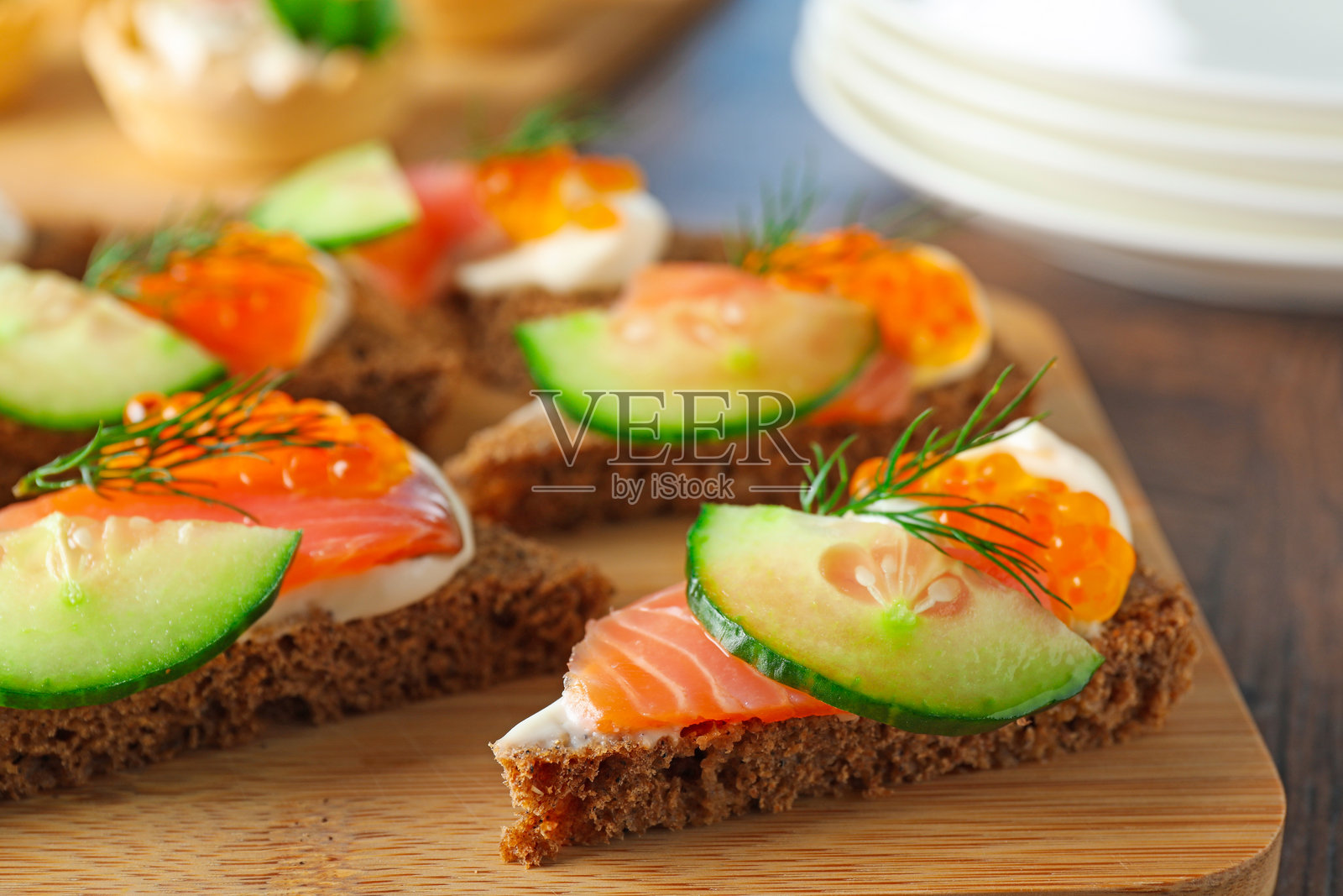 木制桌上摆放着美味的、撒有三文鱼和黄瓜的开胃小吃,特写镜头照片摄影图片