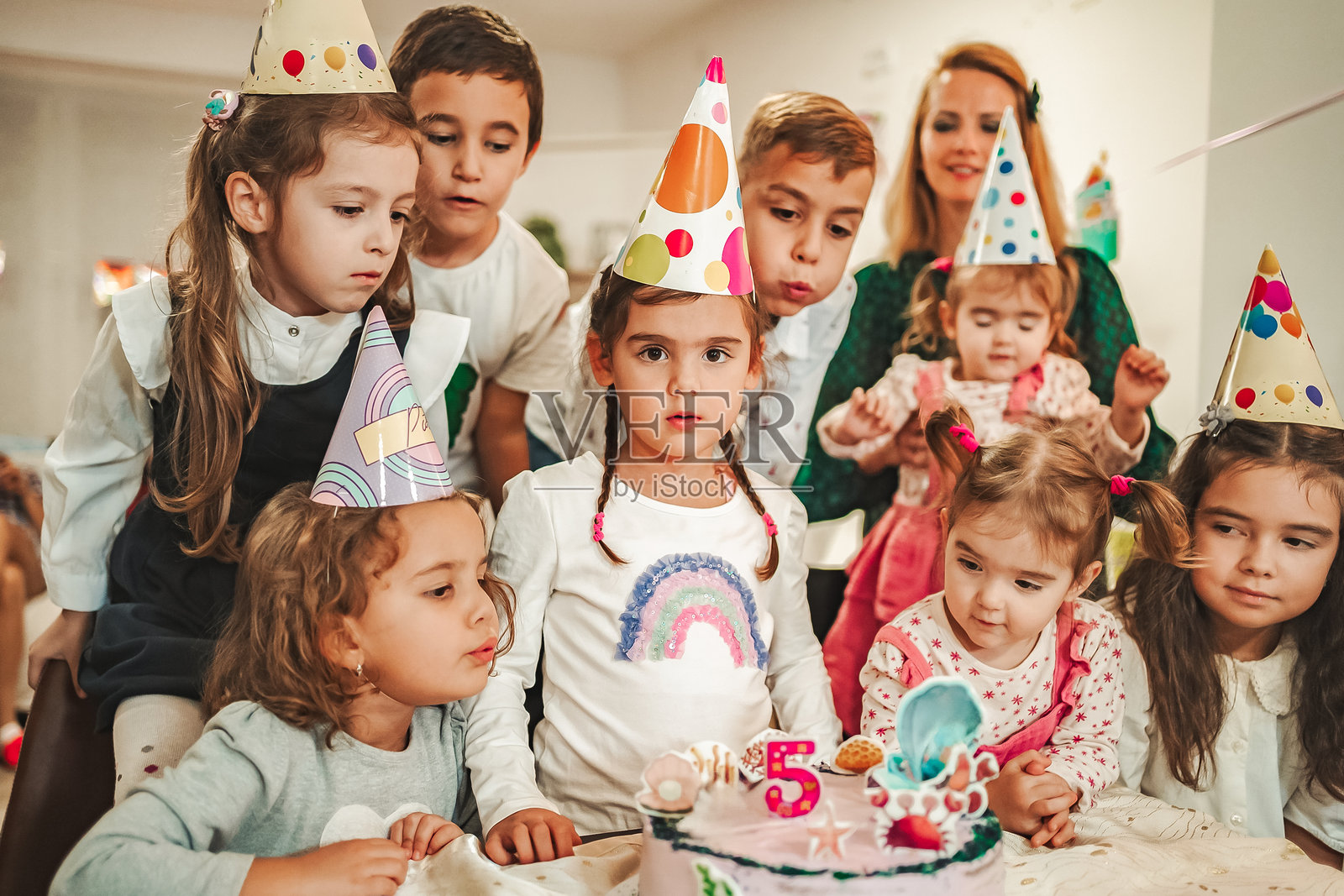 戴着派对帽的孩子们看着插有五根蜡烛的生日蛋糕照片摄影图片