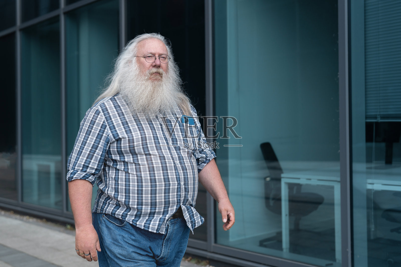一位留着长胡子的老人,在阳光明媚的日子里,走在现代办公楼旁边。照片摄影图片