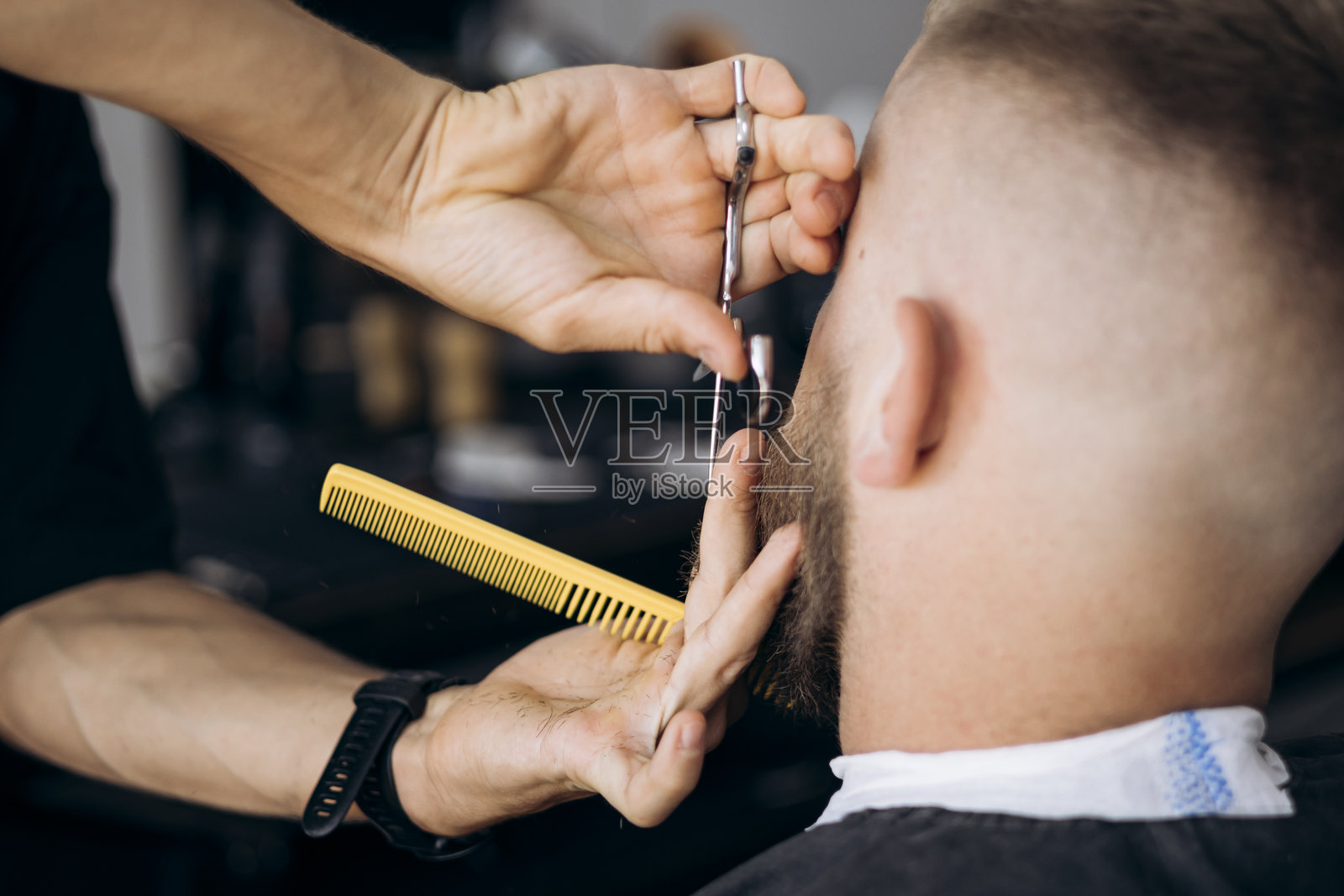理发师在理发店为男性顾客用剪刀和梳子修剪胡须。照片摄影图片