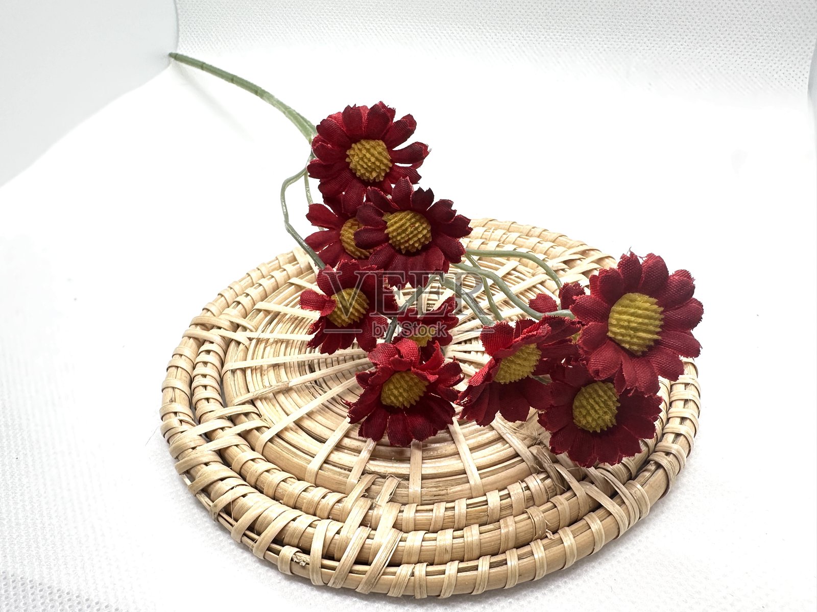 明亮干净的背景下,红色的花朵被精心摆放在编织的竹席上,作为家居装饰或手工材料。照片摄影图片