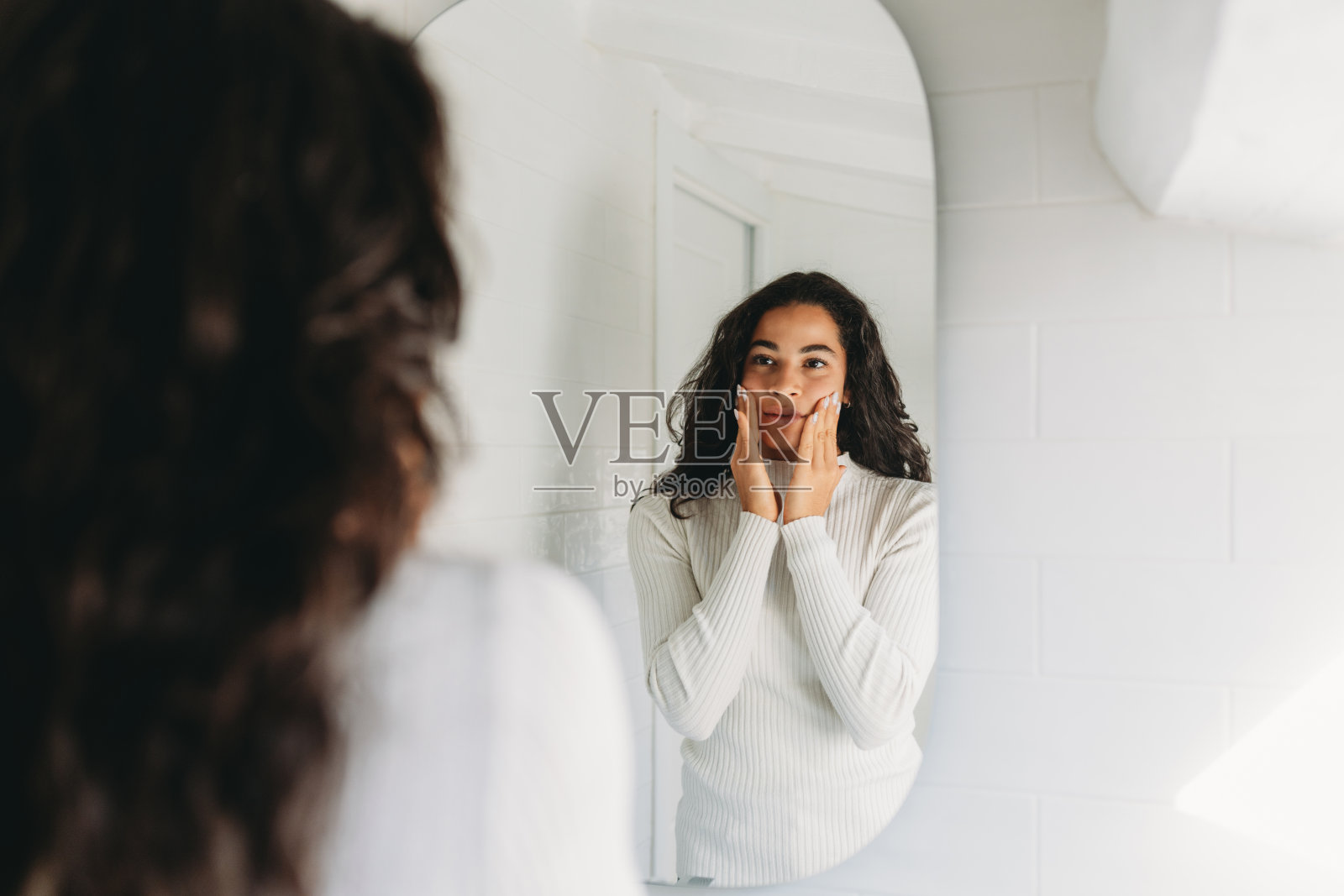 年轻女子在浴室镜子前将护肤品涂抹在脸上照片摄影图片