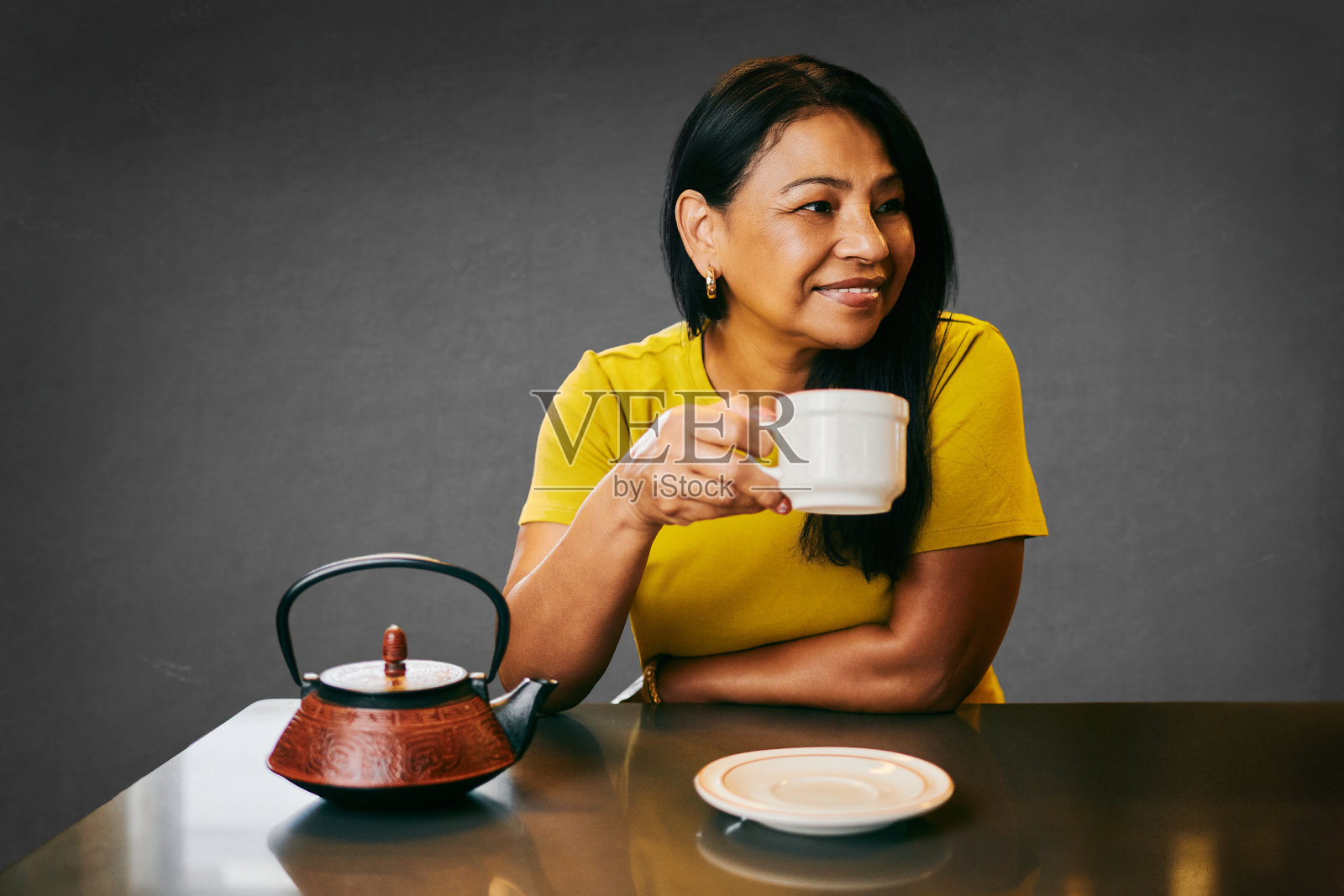 女人在厨房里微笑着喝茶,背景是灰色,这是一个放松的时刻。照片摄影图片