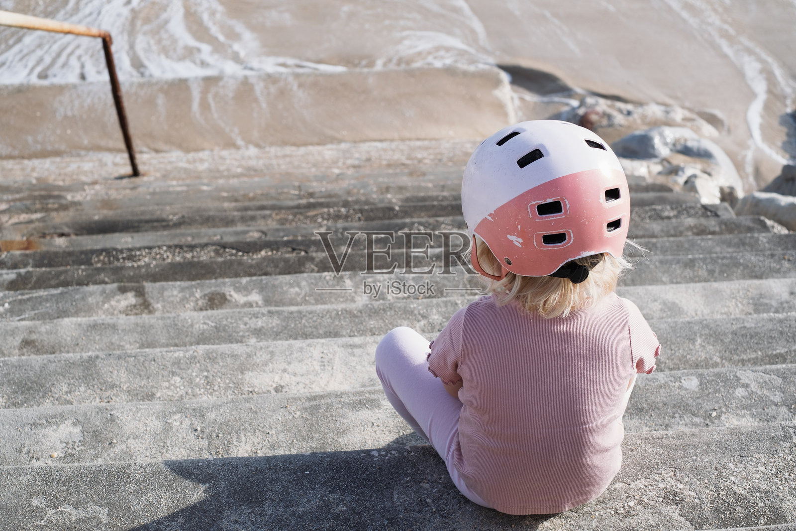 戴着头盔的小女孩坐在楼梯旁,看起来很累照片摄影图片