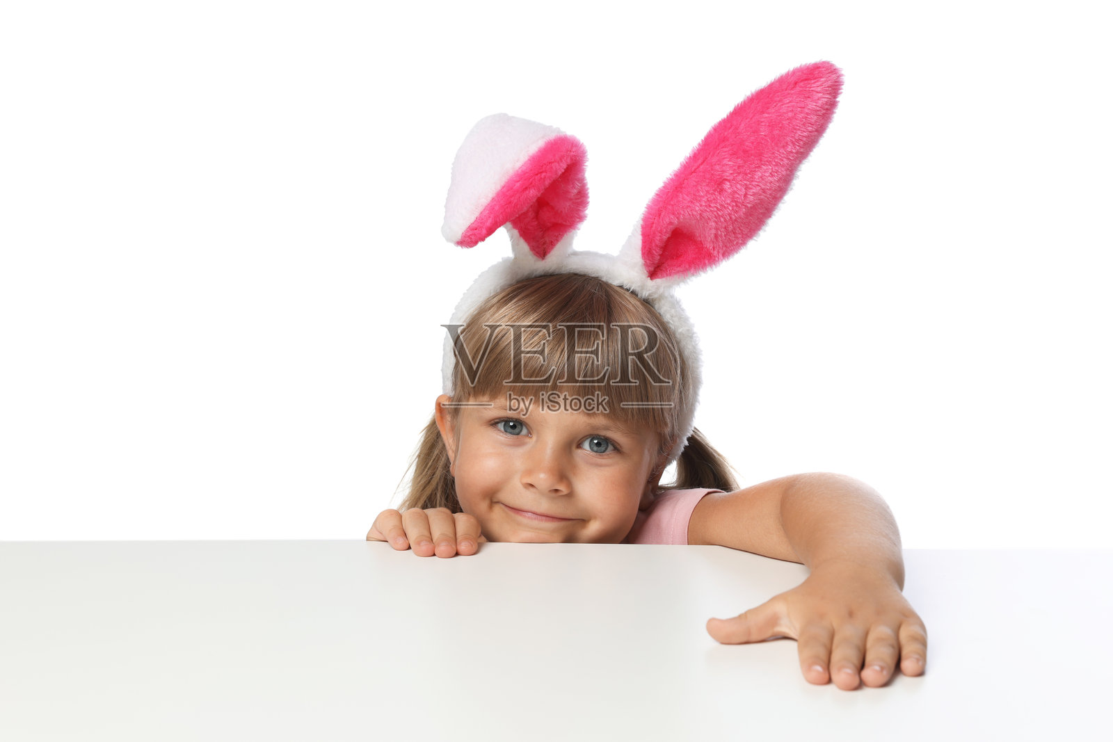 好奇的小女孩戴着兔耳朵,在白背景的桌子边偷偷探出头来照片摄影图片
