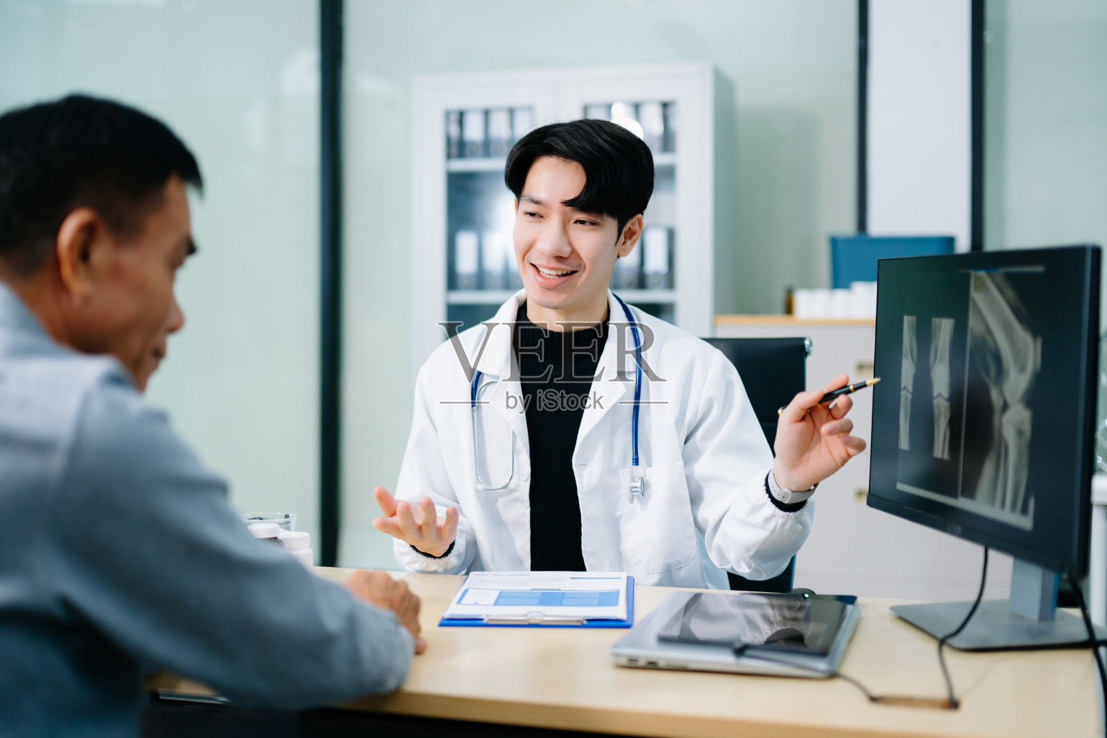 一位亚洲医生在现代诊所里,与一位年长患者讨论膝盖X光片结果。骨科咨询、骨骼护理、健康诊断的概念照片摄影图片