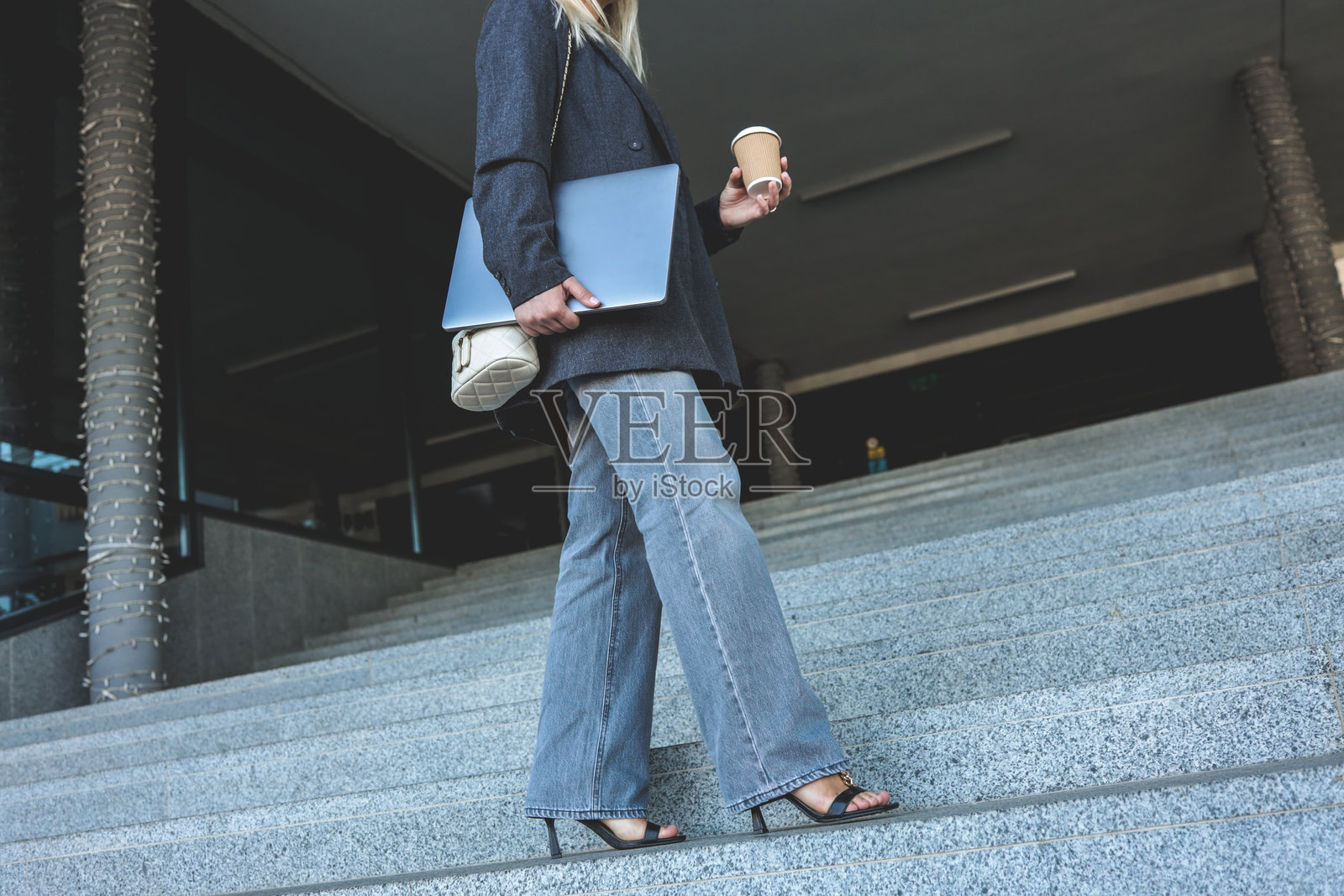 一位时尚的女士,一手拿着咖啡,一手拿着笔记本电脑,走在楼梯上照片摄影图片