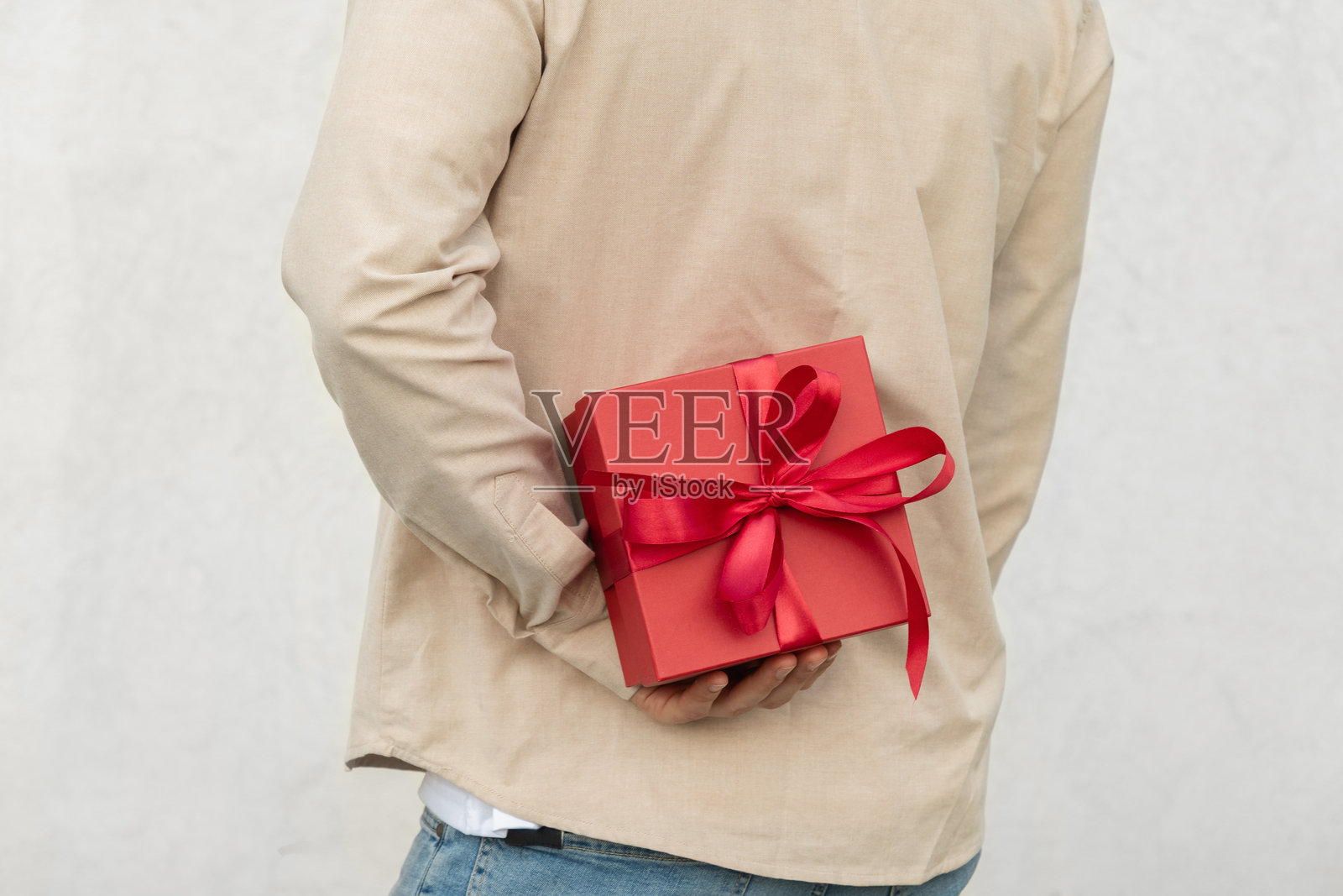 一个人把带着丝带的红色礼物盒藏在身后。情人节。照片摄影图片