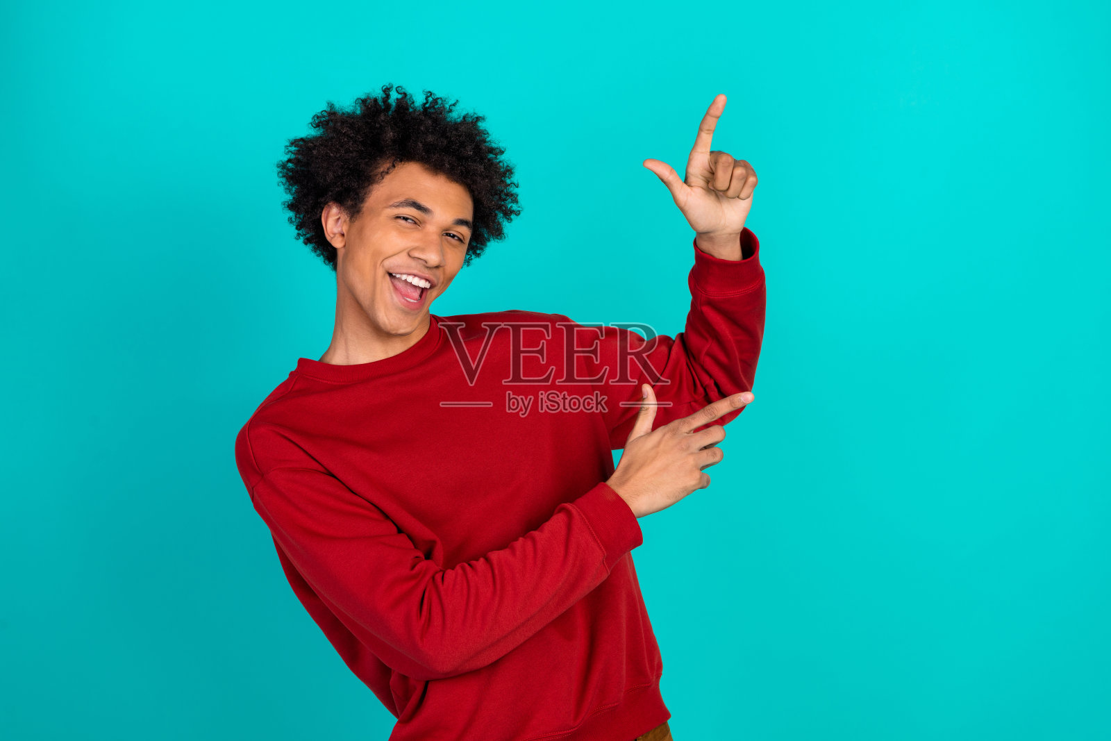 身穿红色毛衣的年轻男子精力充沛,在蓝绿色背景前俏皮地摆出姿势,展示休闲时尚照片摄影图片