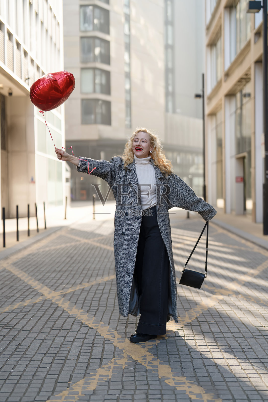 一位女子在城市背景中,手持心形气球,喜悦地庆祝照片摄影图片