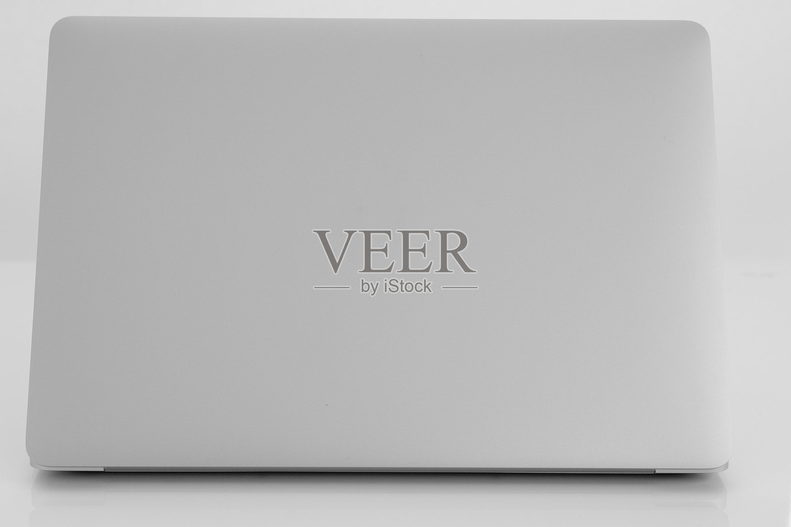 银色笔记本电脑合盖,放置在反光白色的表面上照片摄影图片