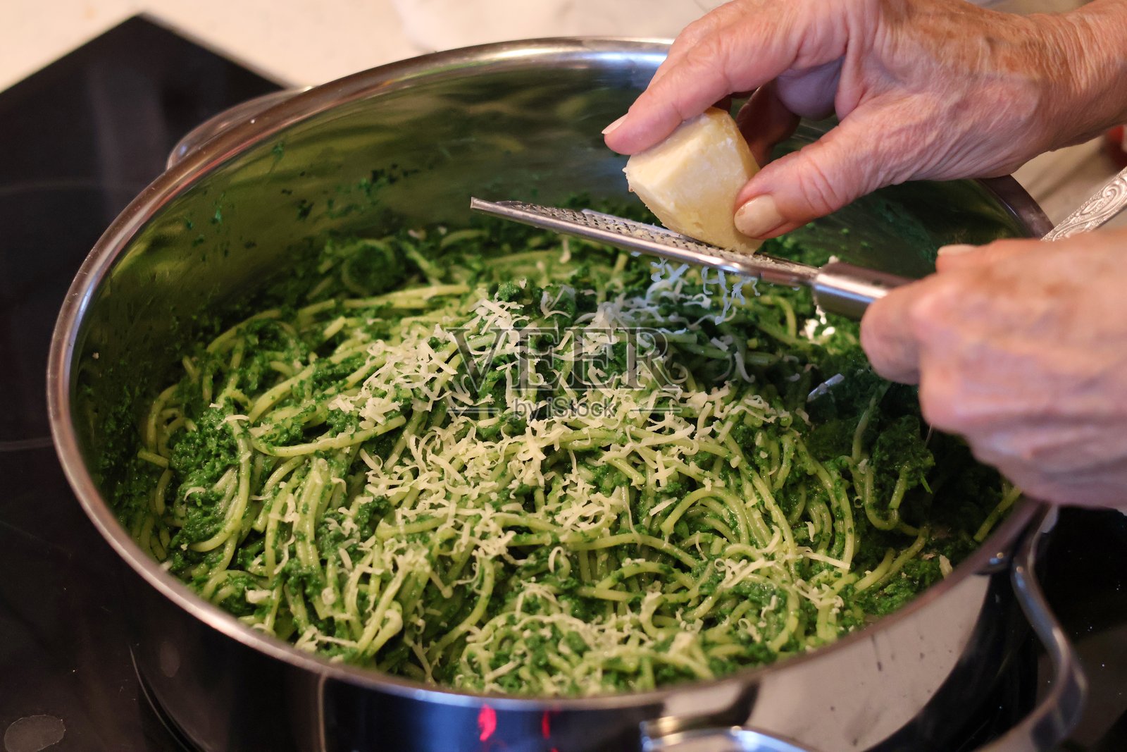 制作菠菜、罗勒、青豆和欧芹香蒜酱意面的过程:锅中混合了橄榄油和大蒜的叶子,正在加入磨碎的奶酪照片摄影图片