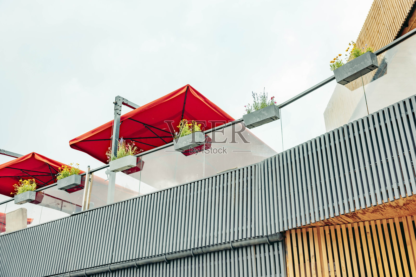 现代建筑,拥有木质外墙和金属点缀。红色雨伞和绿色植物装饰着屋顶露台。整个场景暗示着山区的一个休闲空间。照片摄影图片