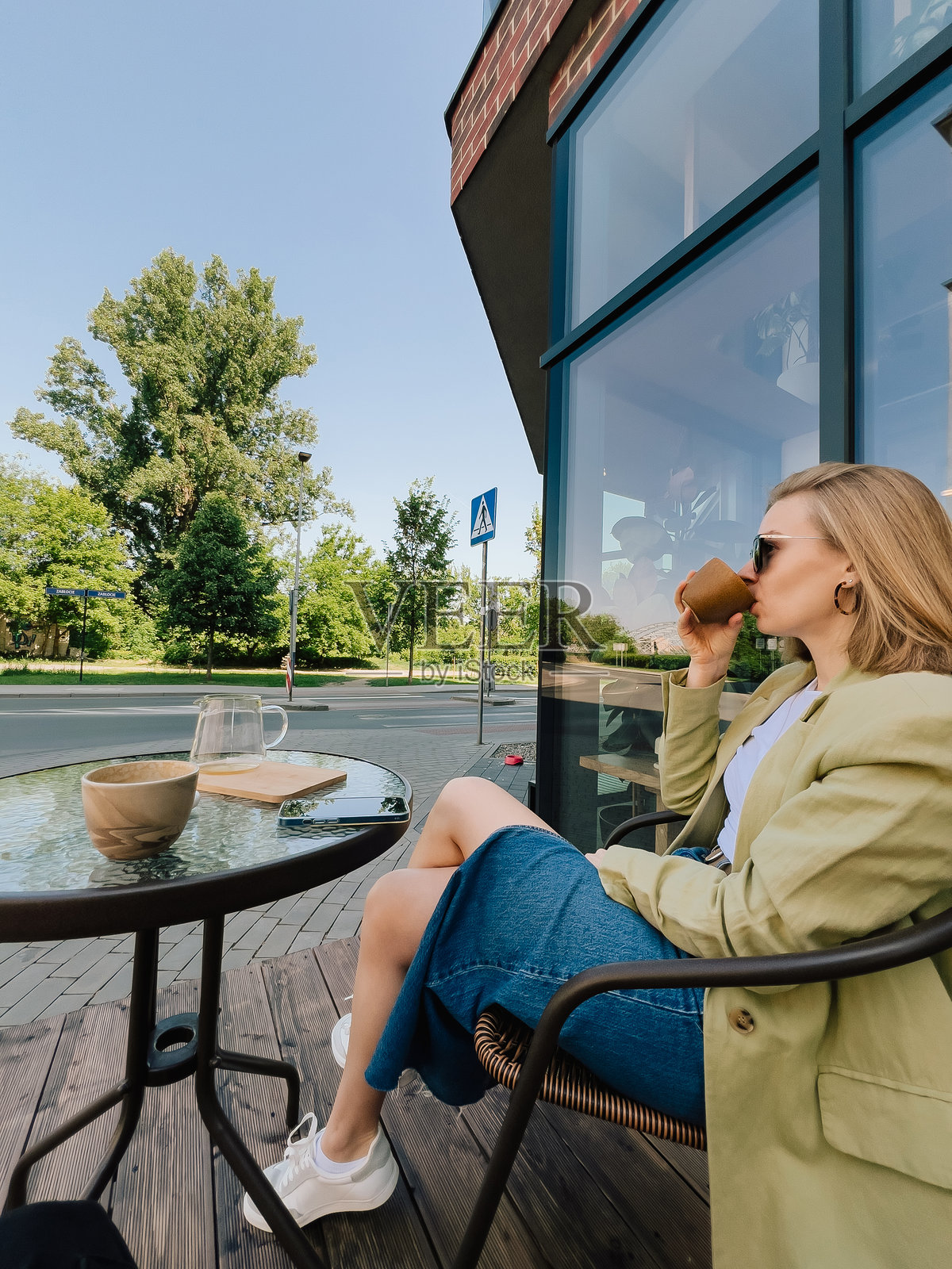 年轻的女商人坐在桌子旁,在繁华的咖啡馆外,喝着咖啡,享受着阳光明媚的一天中来之不易的休息时光,沉浸在充满活力的氛围中。优雅的女孩在户外咖啡馆享受咖啡休息时间。照片摄影图片