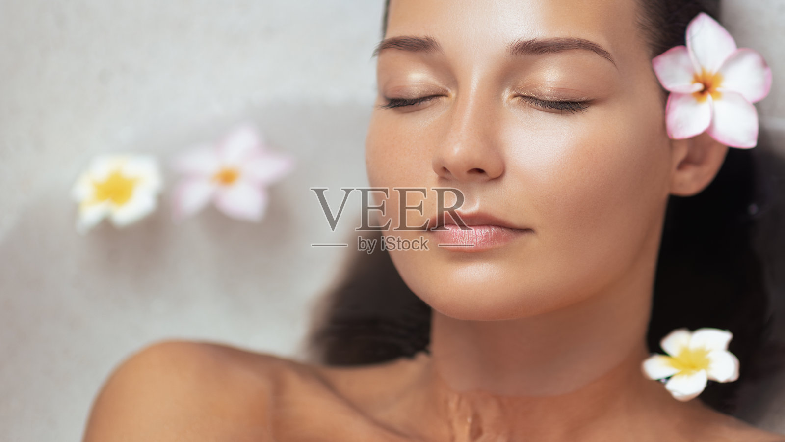 年轻美丽的女子在热带石头浴缸里,周围点缀着鲜花,悠闲地放松照片摄影图片