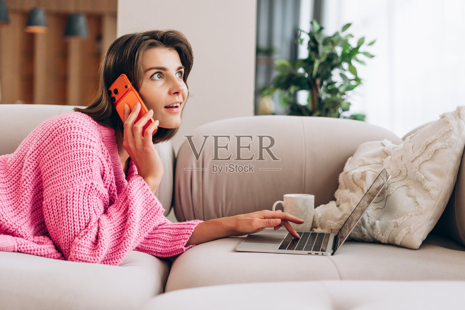 女性在家中多任务处理,一边打电话一边使用笔记本电脑照片摄影图片