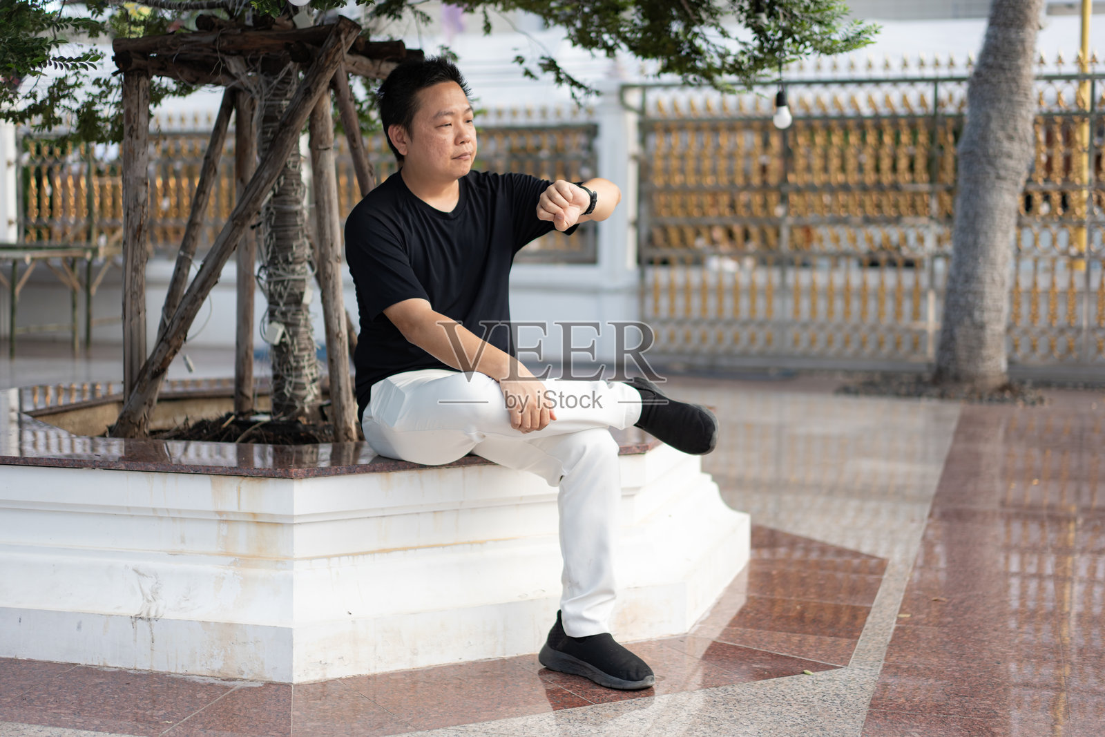 一位旅行者在寺庙前稍作休息,坐在树下看时间,然后继续他的文化之旅。照片摄影图片