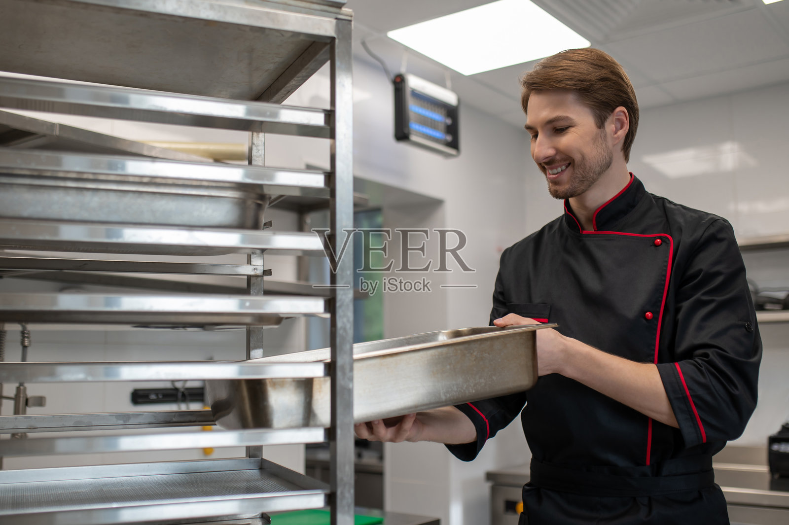 厨师在餐厅厨房将金属烤盘插入烤架照片摄影图片