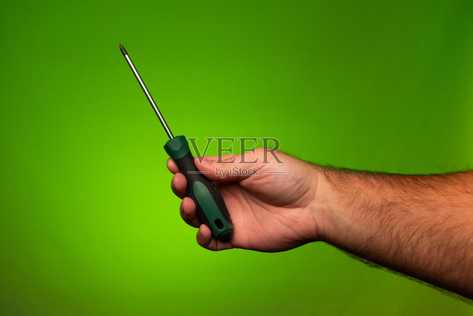 一个人手里拿着一个绿色的飞利浦螺丝刀。一个人拿着飞利浦螺丝刀。绿色的飞利浦螺丝刀照片摄影图片