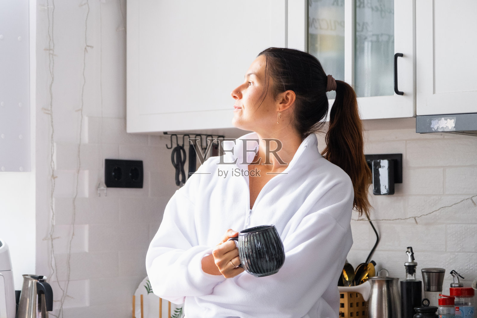 一位女士在厨房里站着喝早晨的咖啡,并望着窗外照片摄影图片