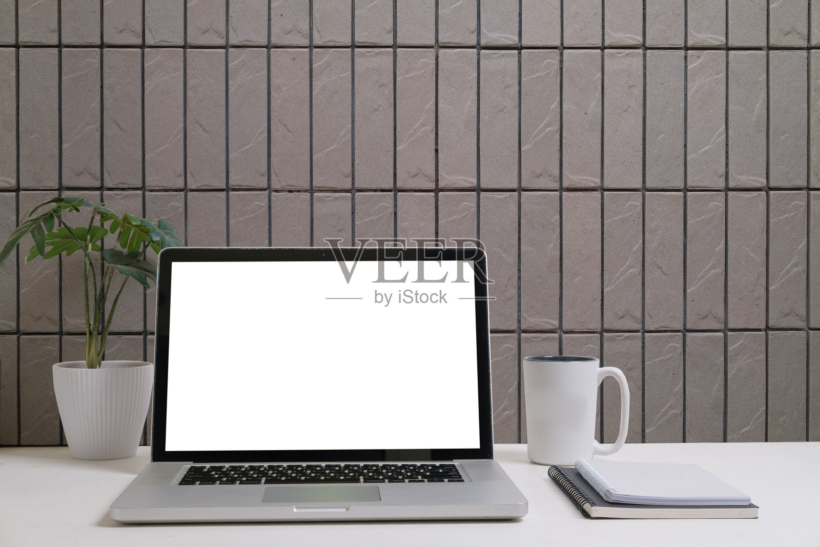 干净简约的办公空间,配有笔记本电脑、咖啡杯、铅笔和笔记本,背景是瓷砖墙。照片摄影图片