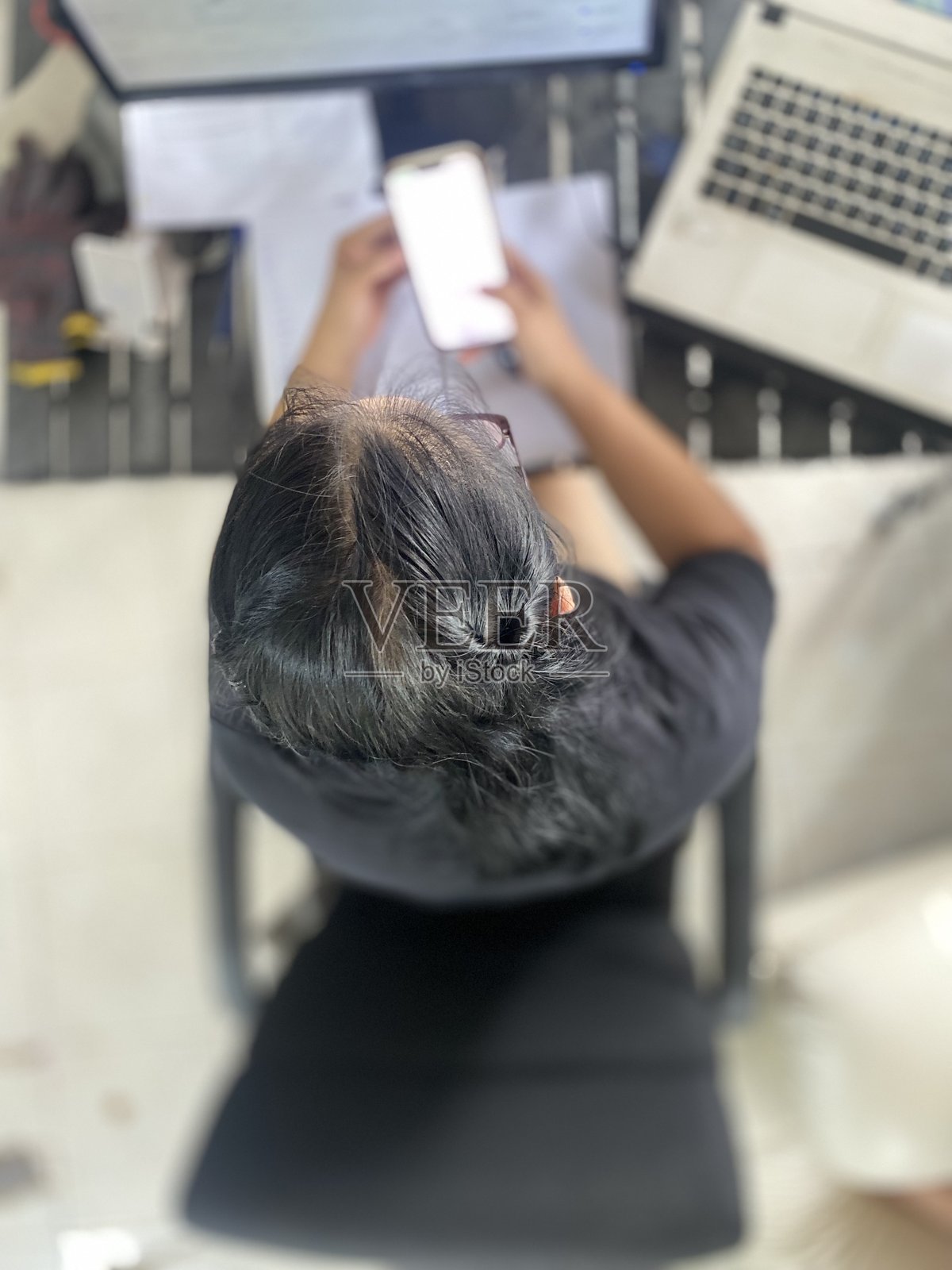 俯视角度显示一个坐着工作的人的发型。照片摄影图片