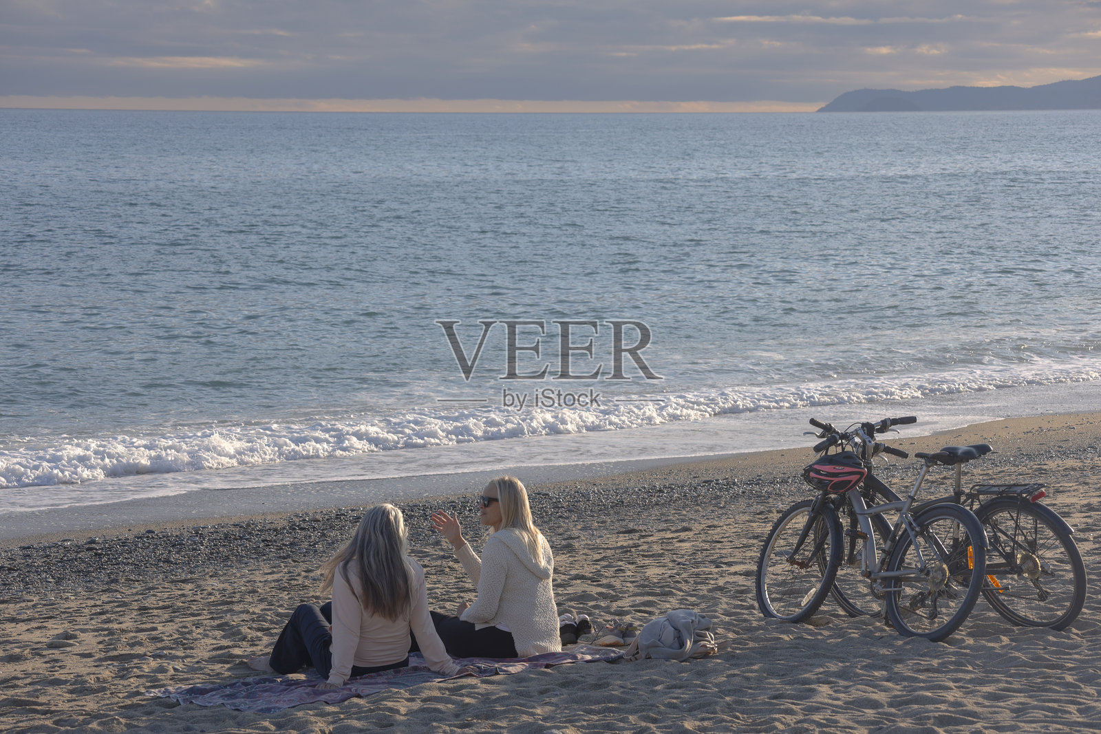 成熟的女性在日落时分的海滩上骑自行车聊天照片摄影图片