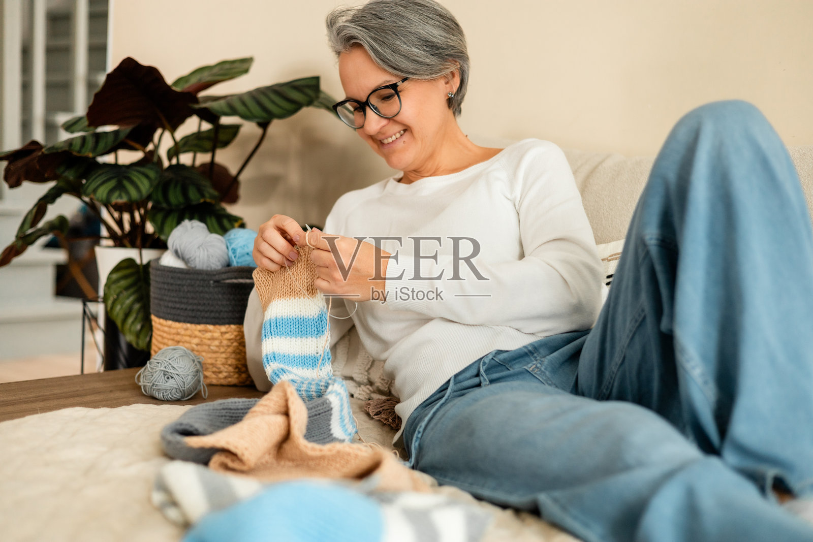 一位微笑的老年女性在家中舒适地放松,同时编织着色彩鲜艳的羊毛织物照片摄影图片