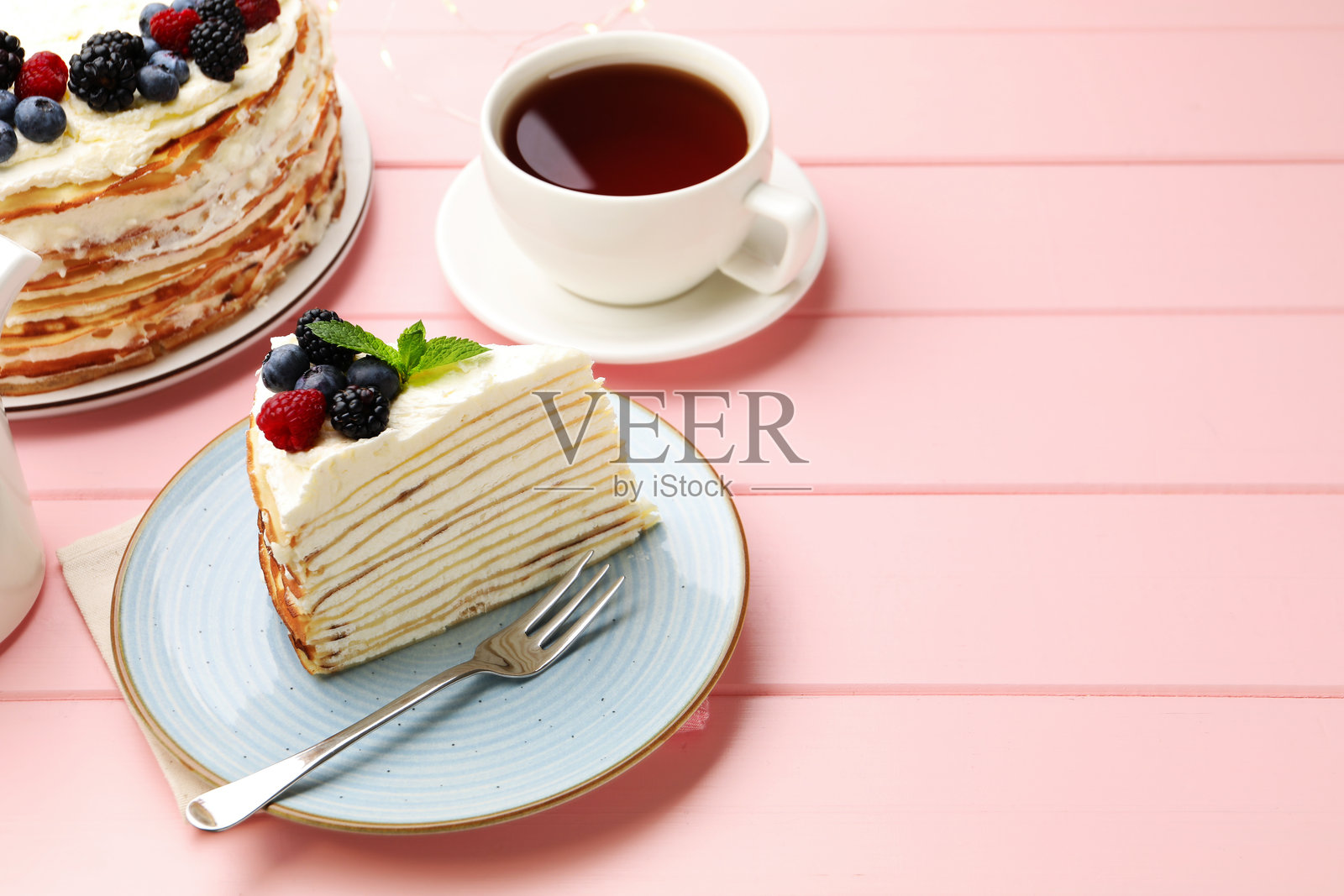 粉色木桌上摆放着一块美味的千层蛋糕,上面有浆果,特写。留有文字空间照片摄影图片