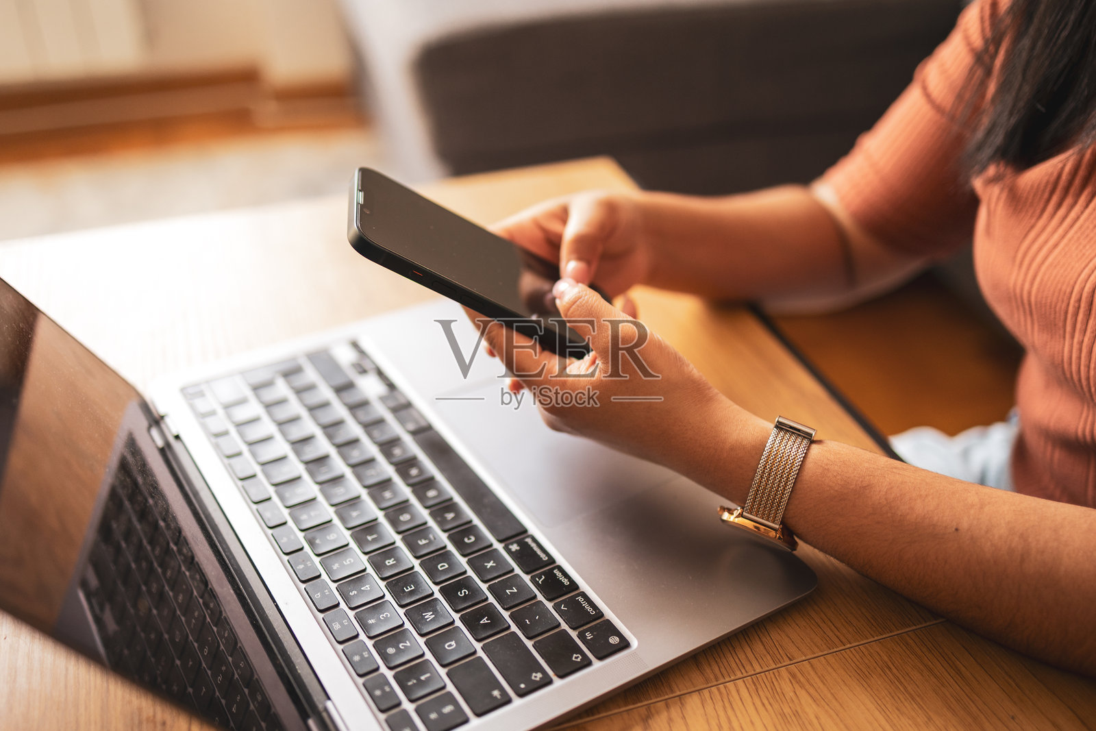 一个人在室内的木制桌子旁使用智能手机和笔记本电脑照片摄影图片