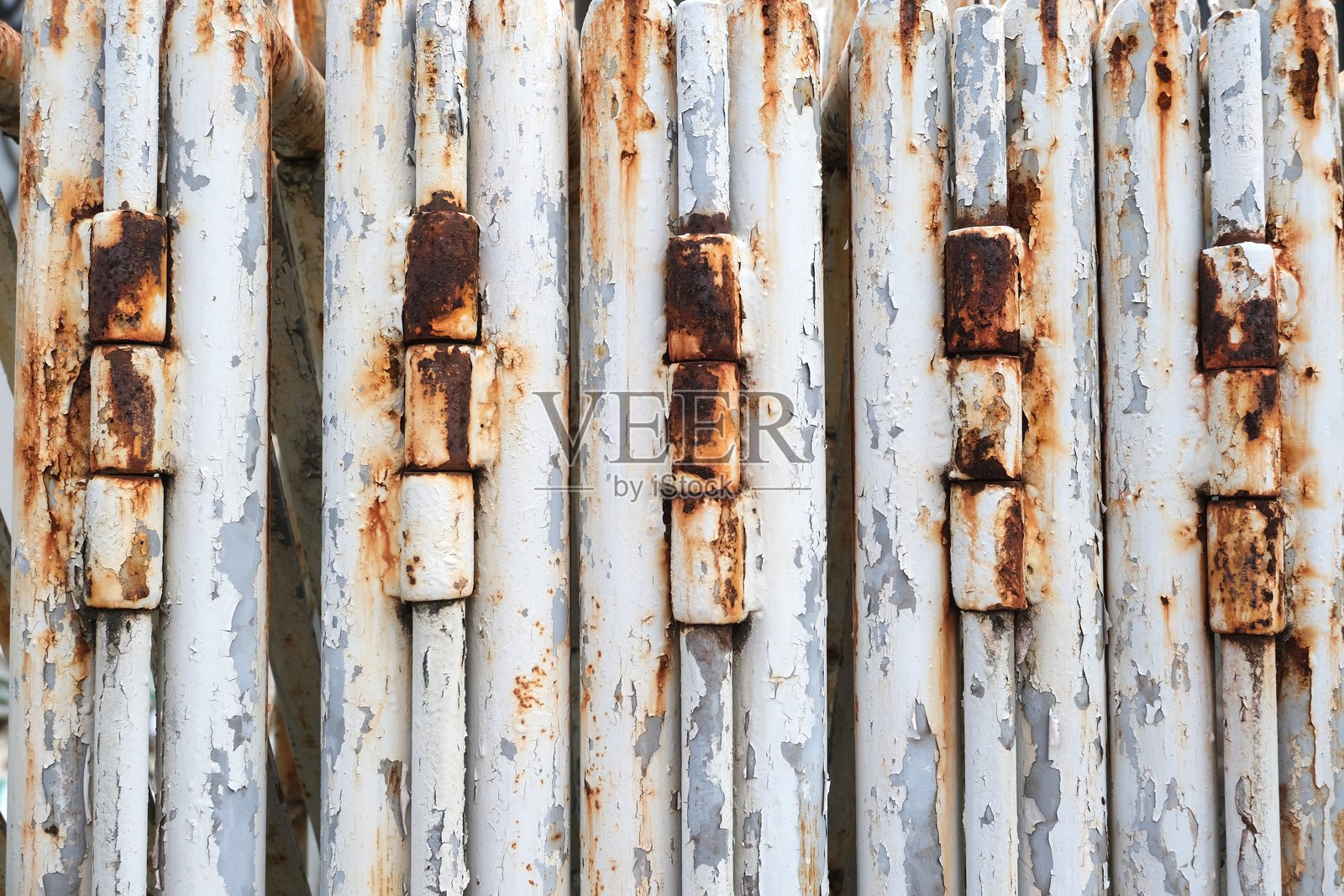 特写镜头,一扇风化、涂有白色油漆的折叠金属门上排列着多个生锈的铰链,显示出腐蚀和老化的痕迹。照片摄影图片