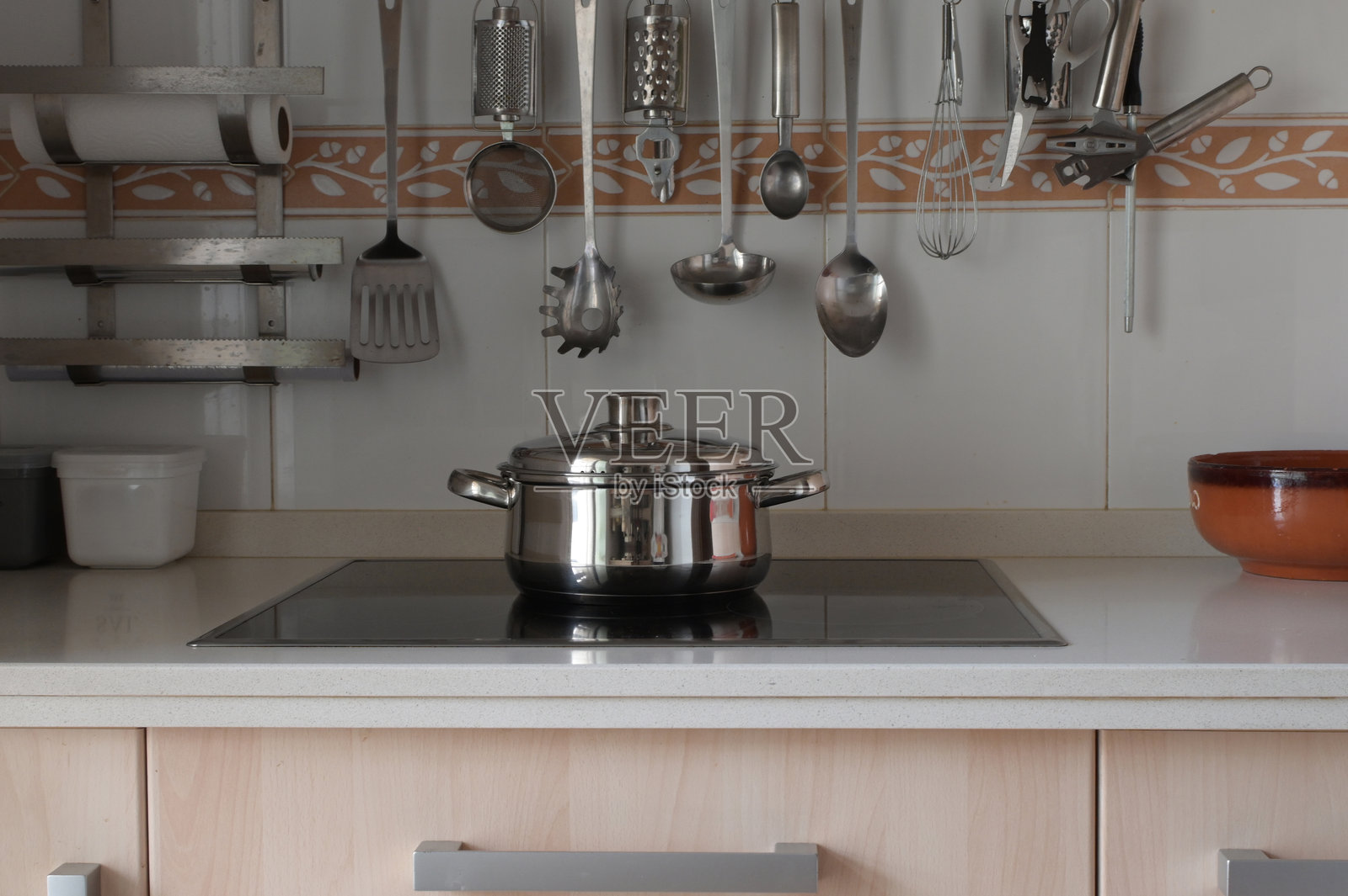 不锈钢锅放在时尚的电磁炉上,上方悬挂着金属厨具和浅木色橱柜,现代洁净的厨房场景,突出锅具、倒影和日常烹饪。照片摄影图片