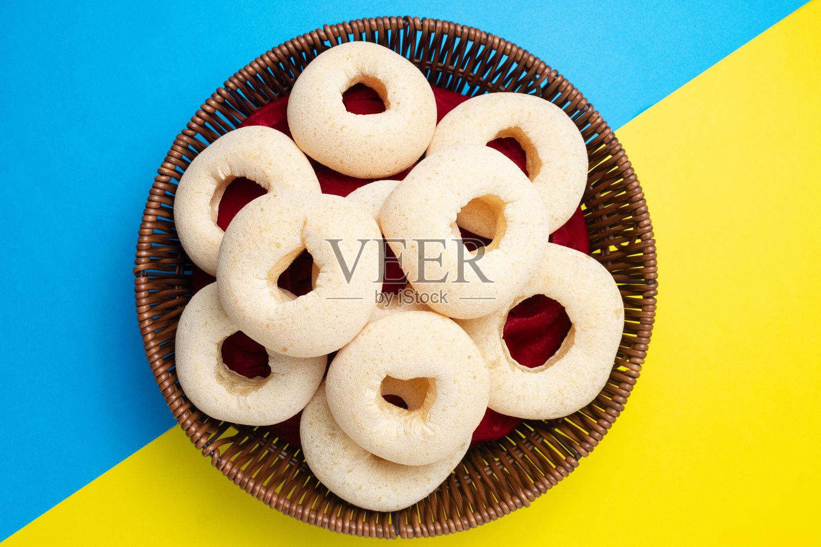 俯视视角,篮子里装满了传统奶酪面包圈(Pandebono 或 Rosquillas),背景为鲜艳的蓝黄分割色。照片摄影图片