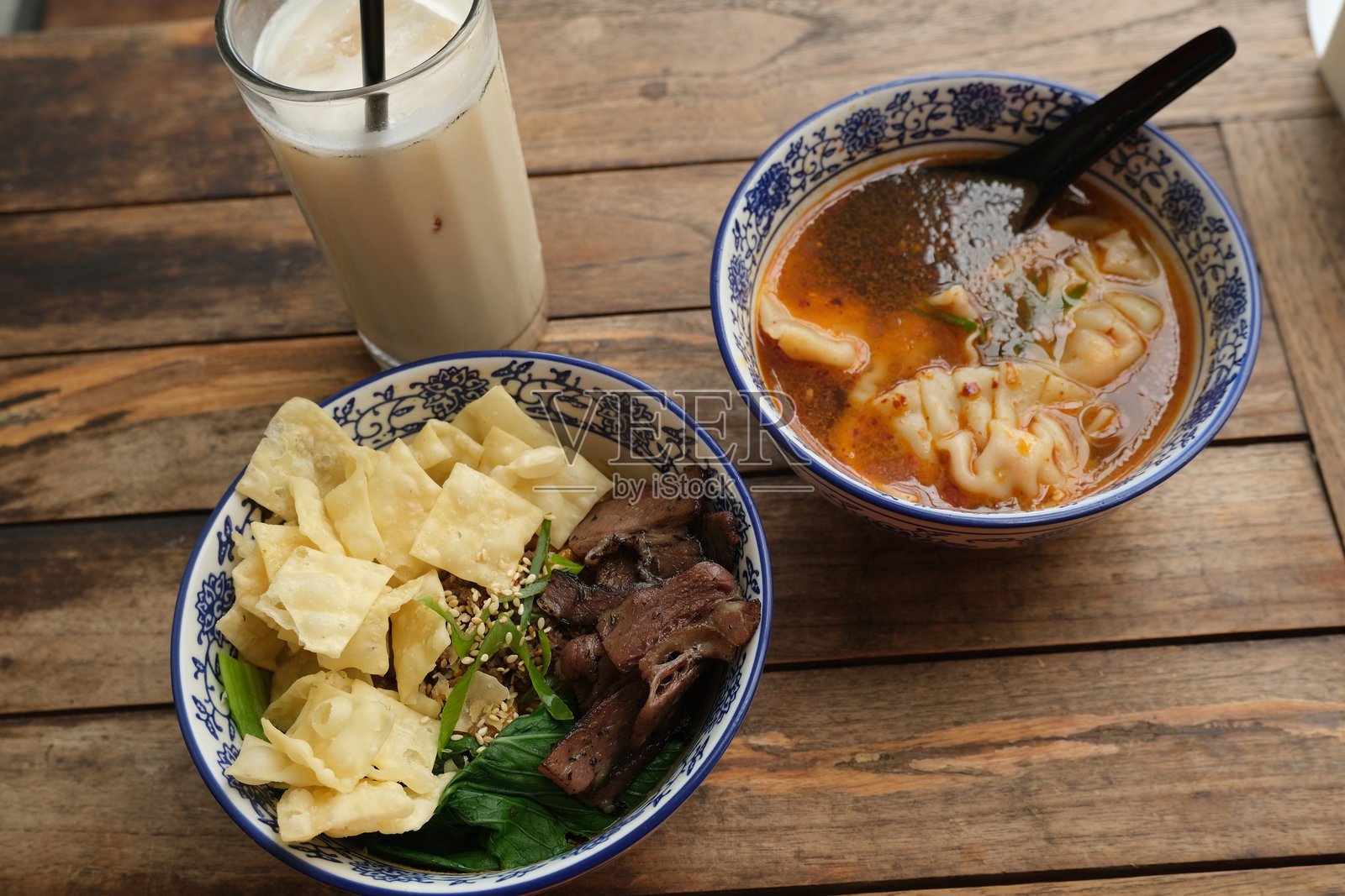 一顿丰盛的亚洲餐,包括一碗干面配烤牛肉和饼干、一碗辛辣的饺子汤以及一杯冰奶茶。照片摄影图片