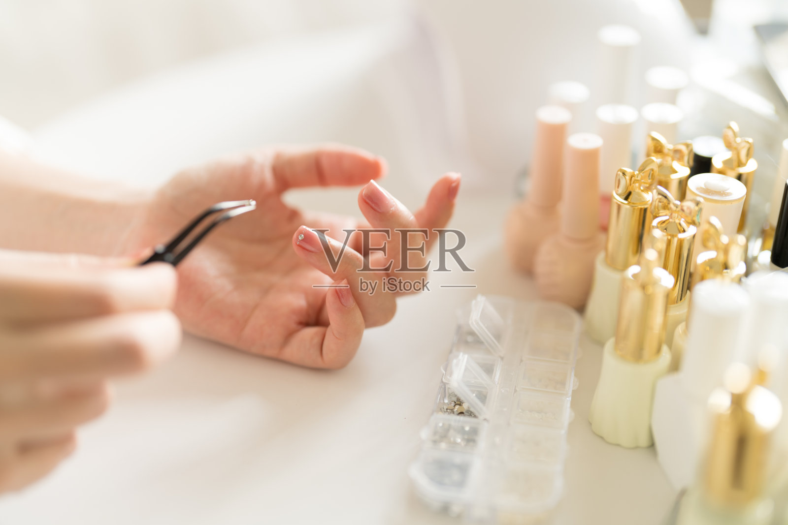 用镊子夹起一颗钻石,然后将其粘在指甲上。照片摄影图片