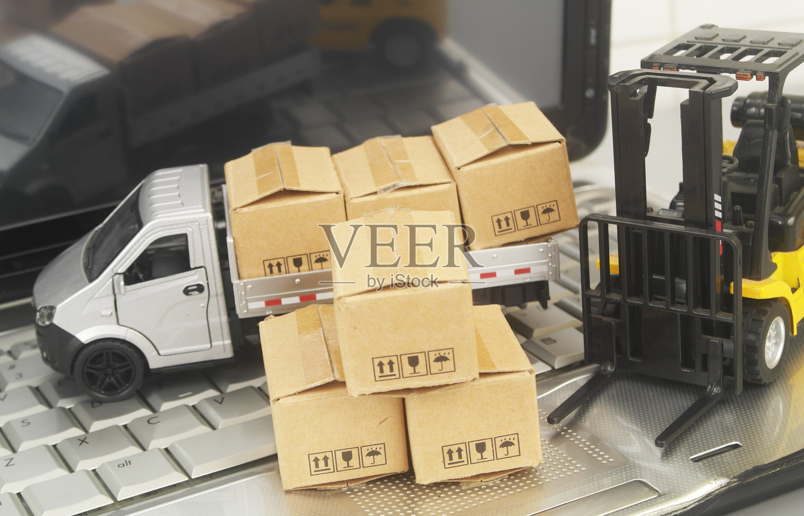 笔记本电脑特写,上面放着卡车、叉车和箱子。照片摄影图片