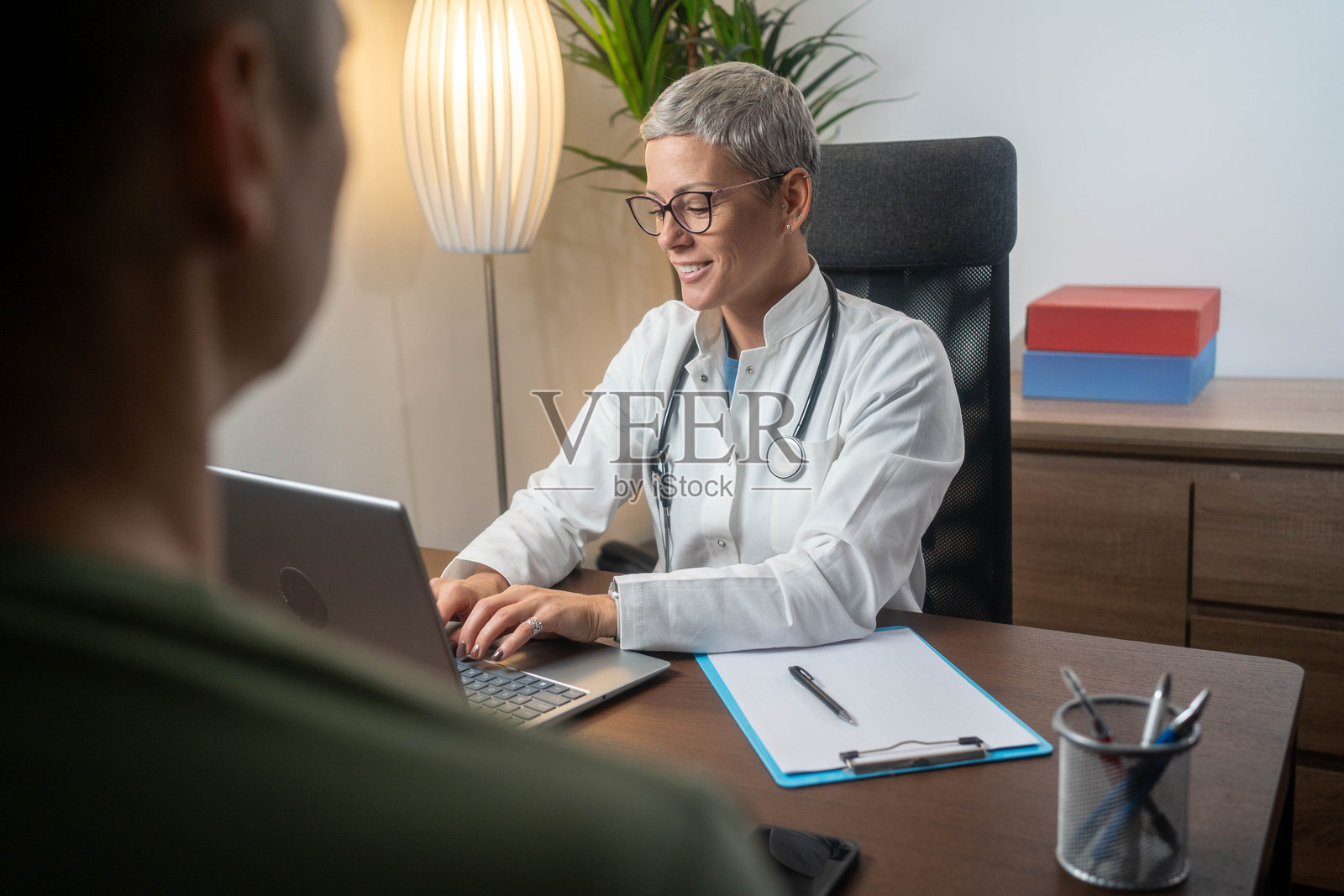 医生在诊所就诊时,使用笔记本电脑咨询病人。照片摄影图片