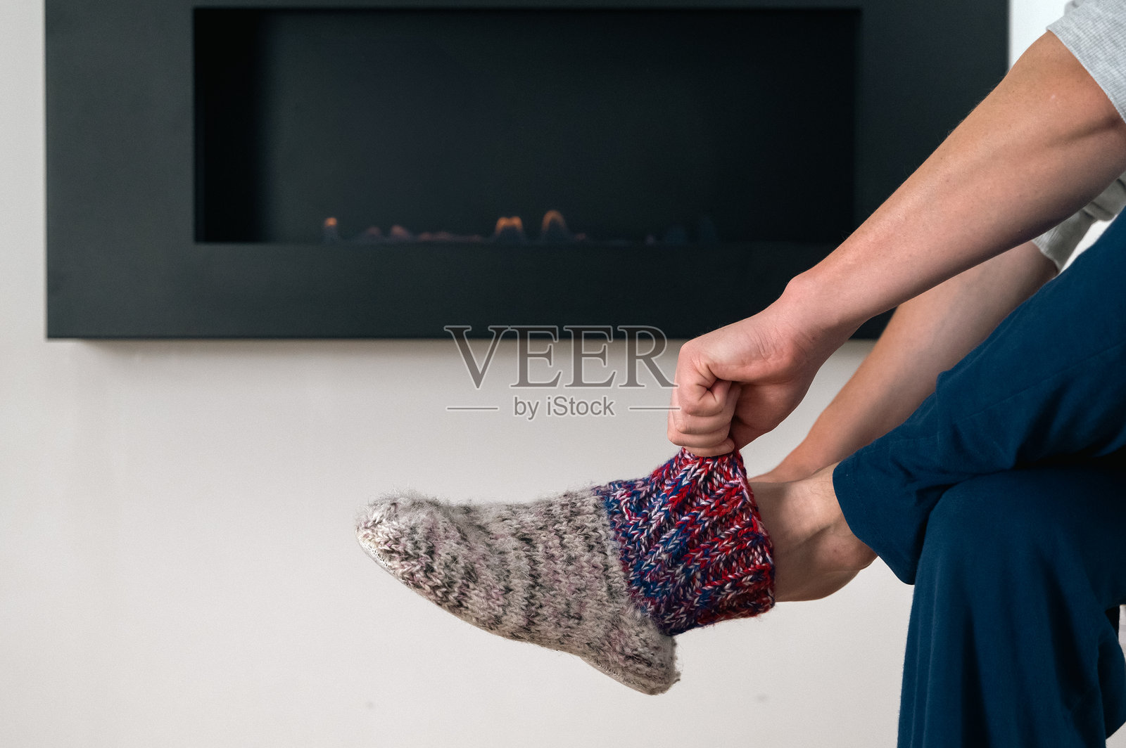 男人在黑色壁炉旁放松,同时穿上手工羊毛袜照片摄影图片